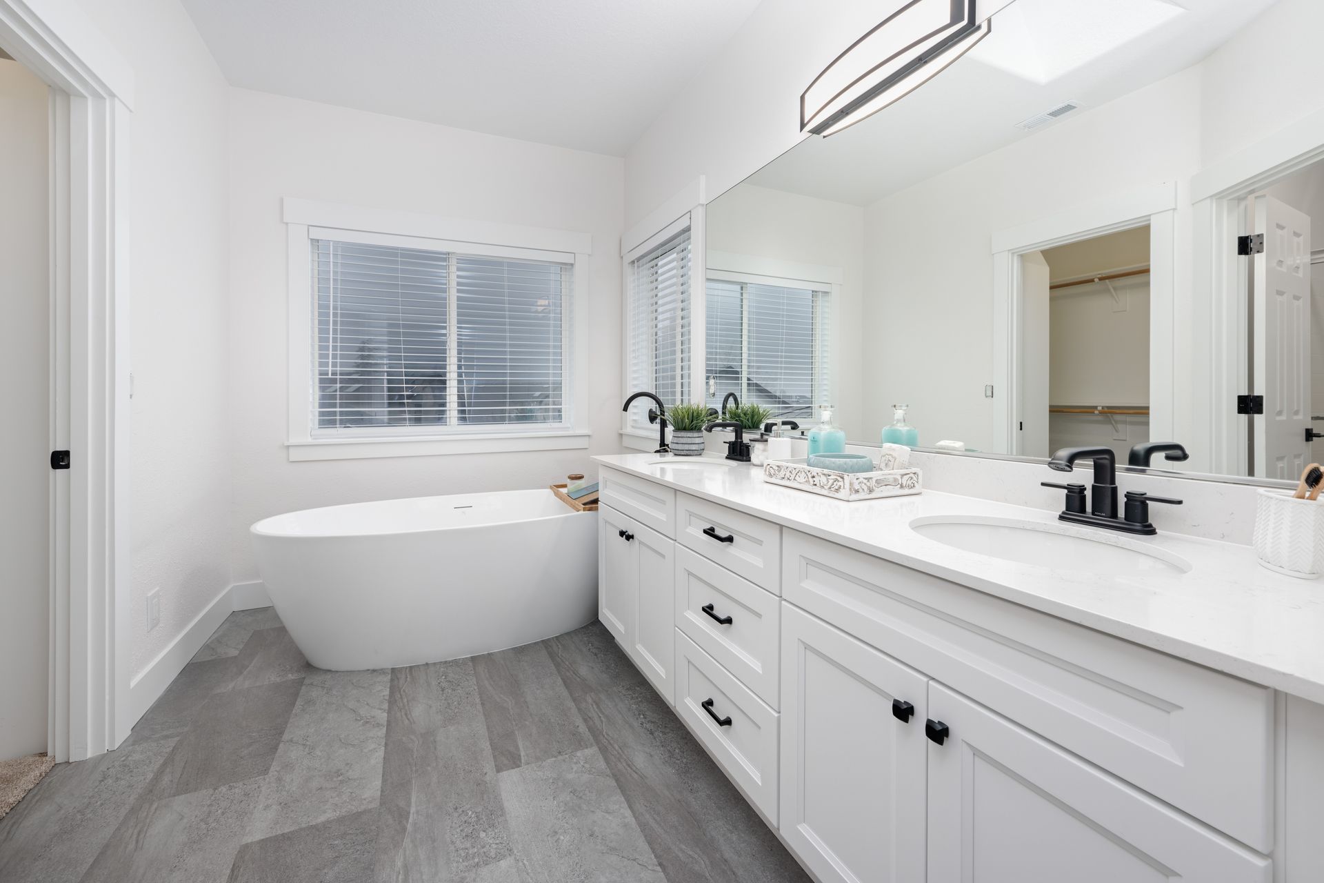 White bathroom with a tub, vanity, and window; gray floor.