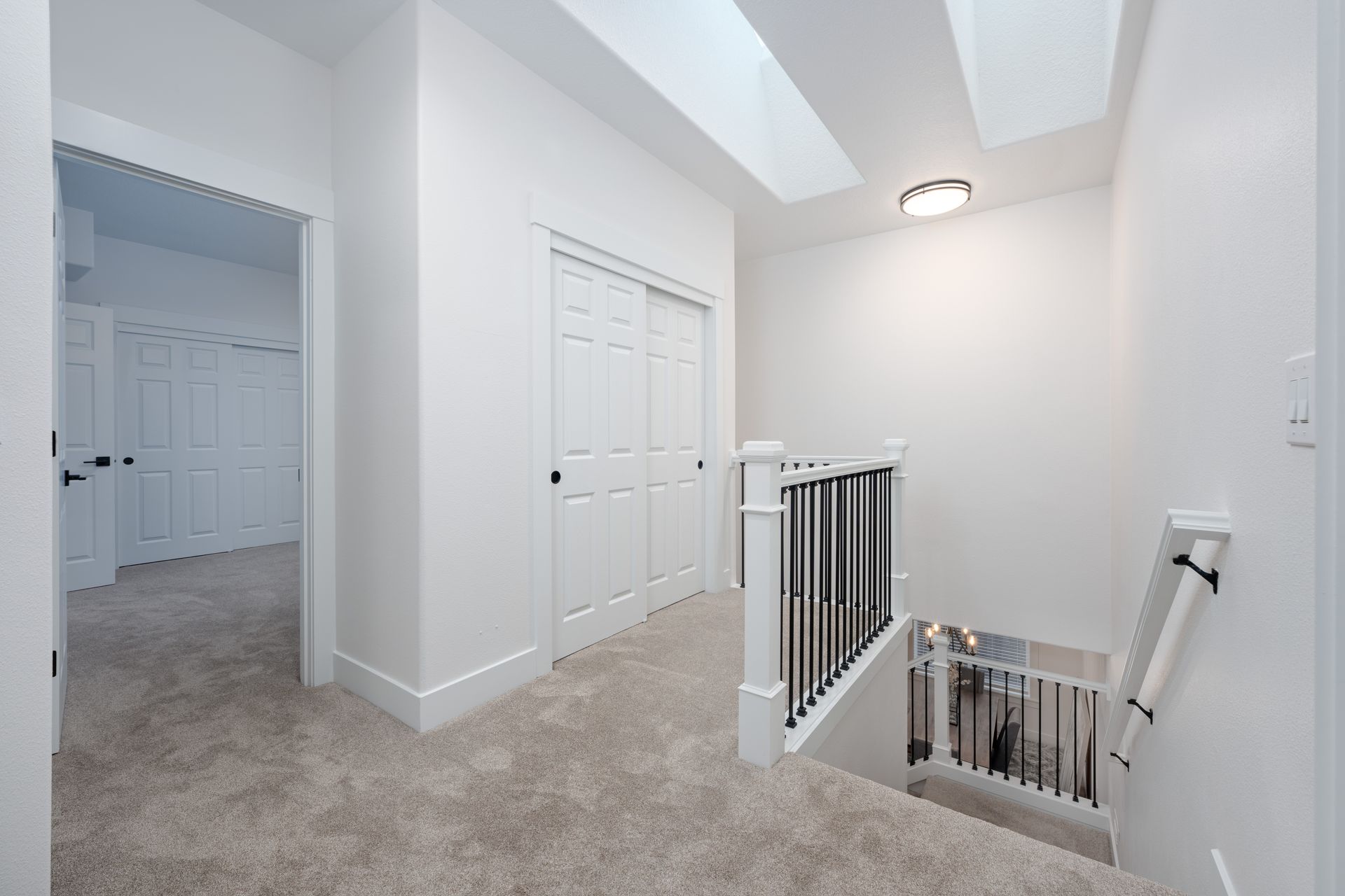 Hallway with carpet, white walls, closet, stairs, and natural light from skylights.