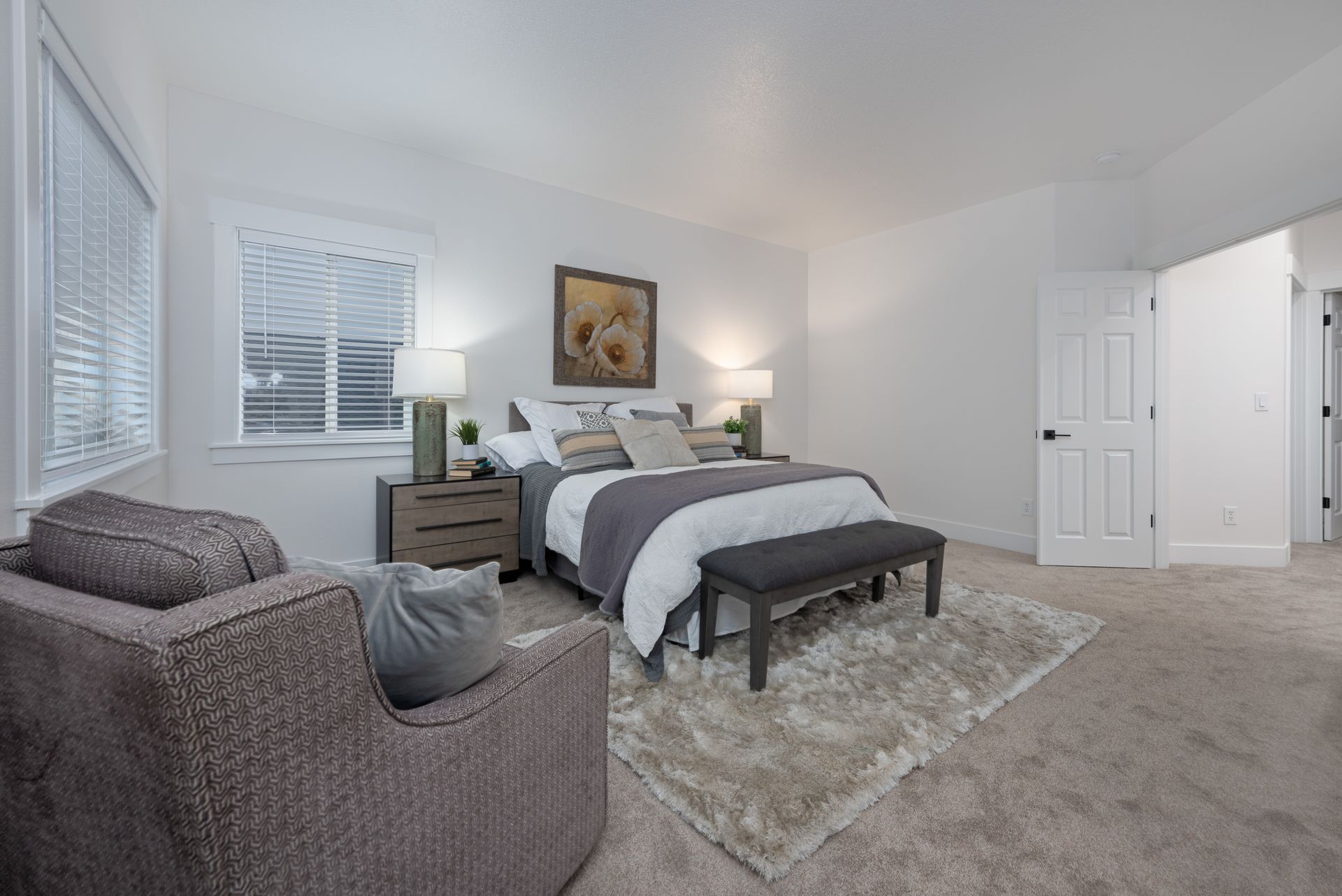 Bedroom with bed, nightstands, armchair, rug, and door, all in neutral colors.