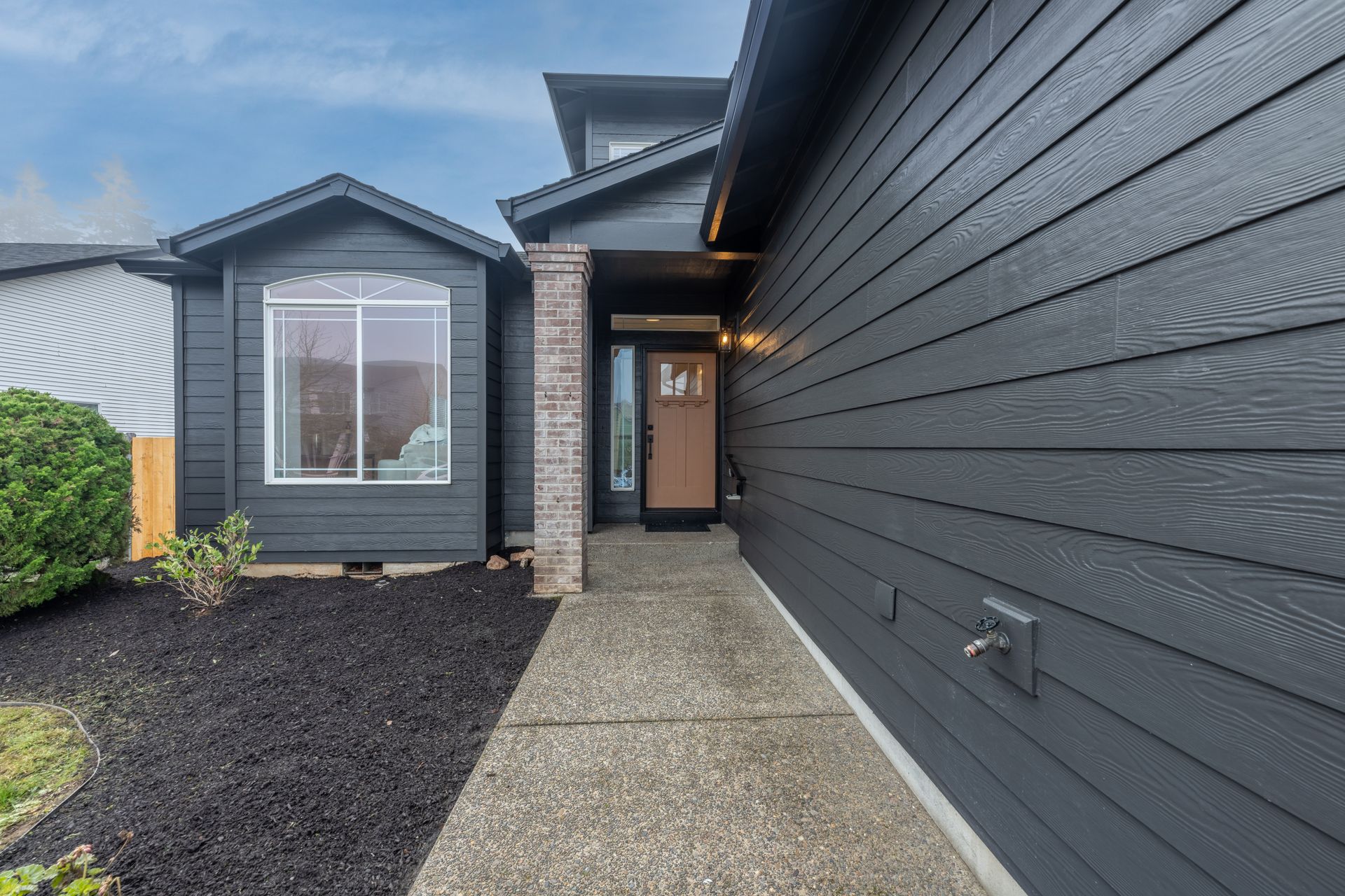 Dark gray house exterior with a covered entryway, gray siding, and bay window.