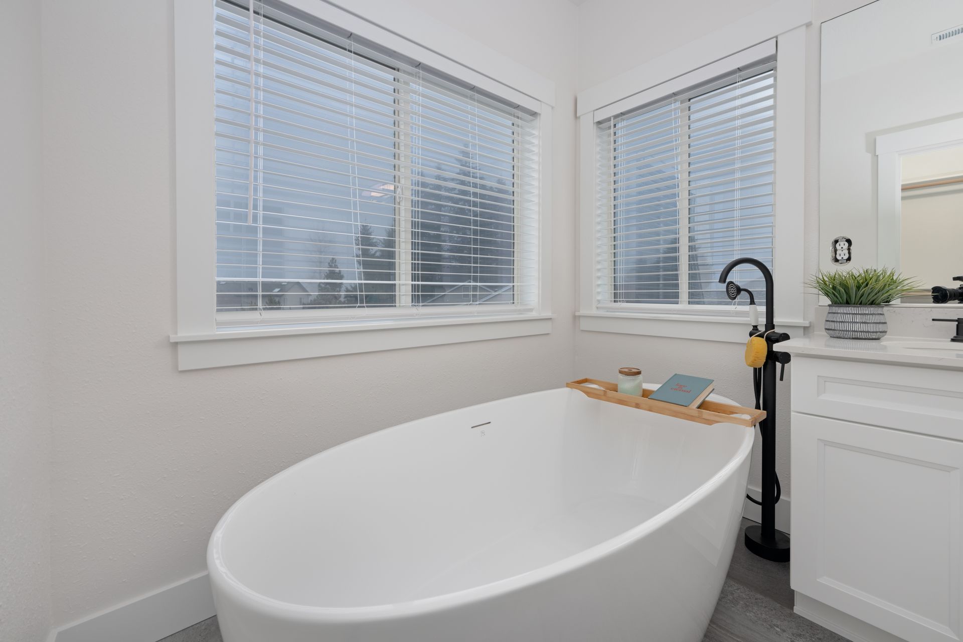 White bathtub in a bright bathroom near windows; a wooden tray holds items.