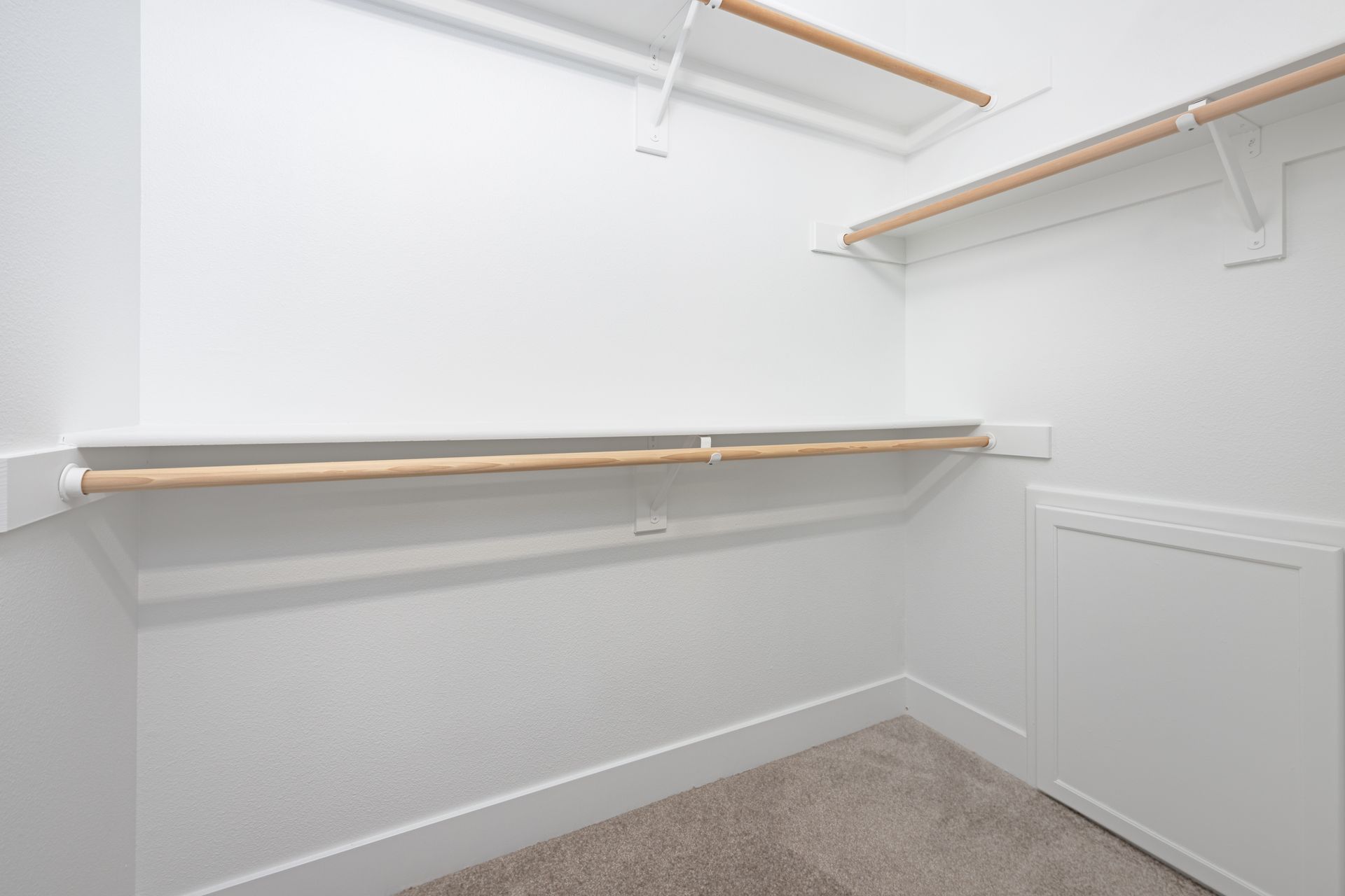 Empty white closet with a carpeted floor, wood shelves, and a storage cabinet.