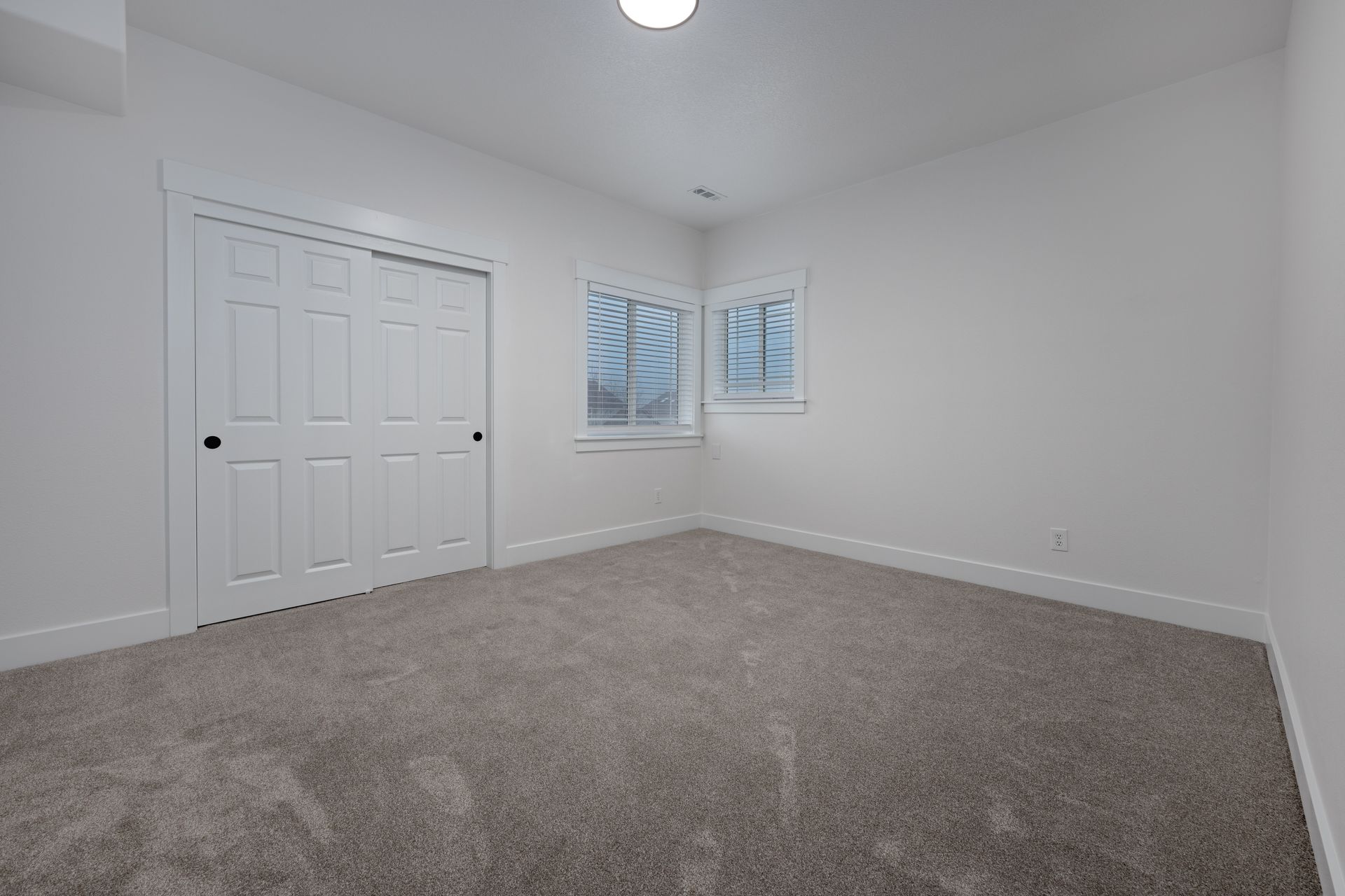Empty bedroom with carpet, white walls, sliding closet doors, and windows.