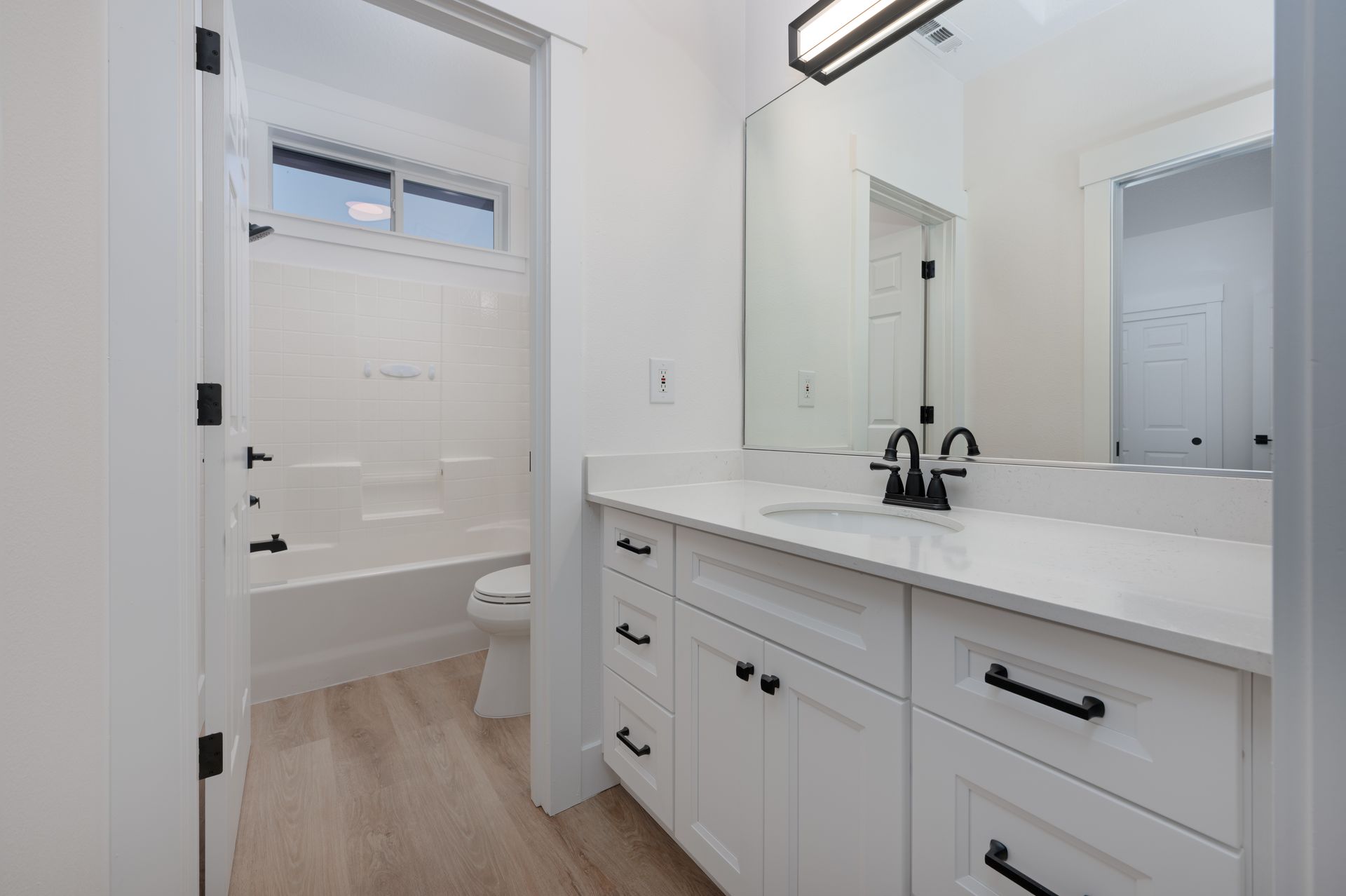 White bathroom with vanity, black fixtures, and open door to a tub/shower.