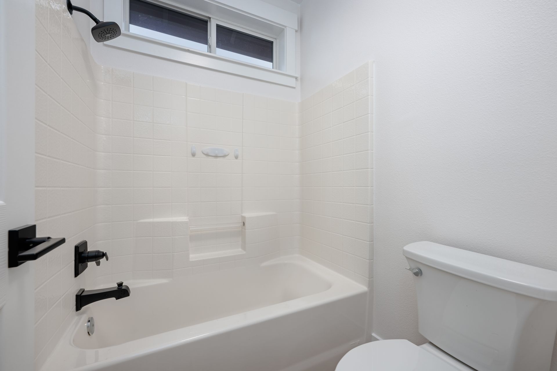 White bathroom with tub, toilet, showerhead, and dark fixtures.