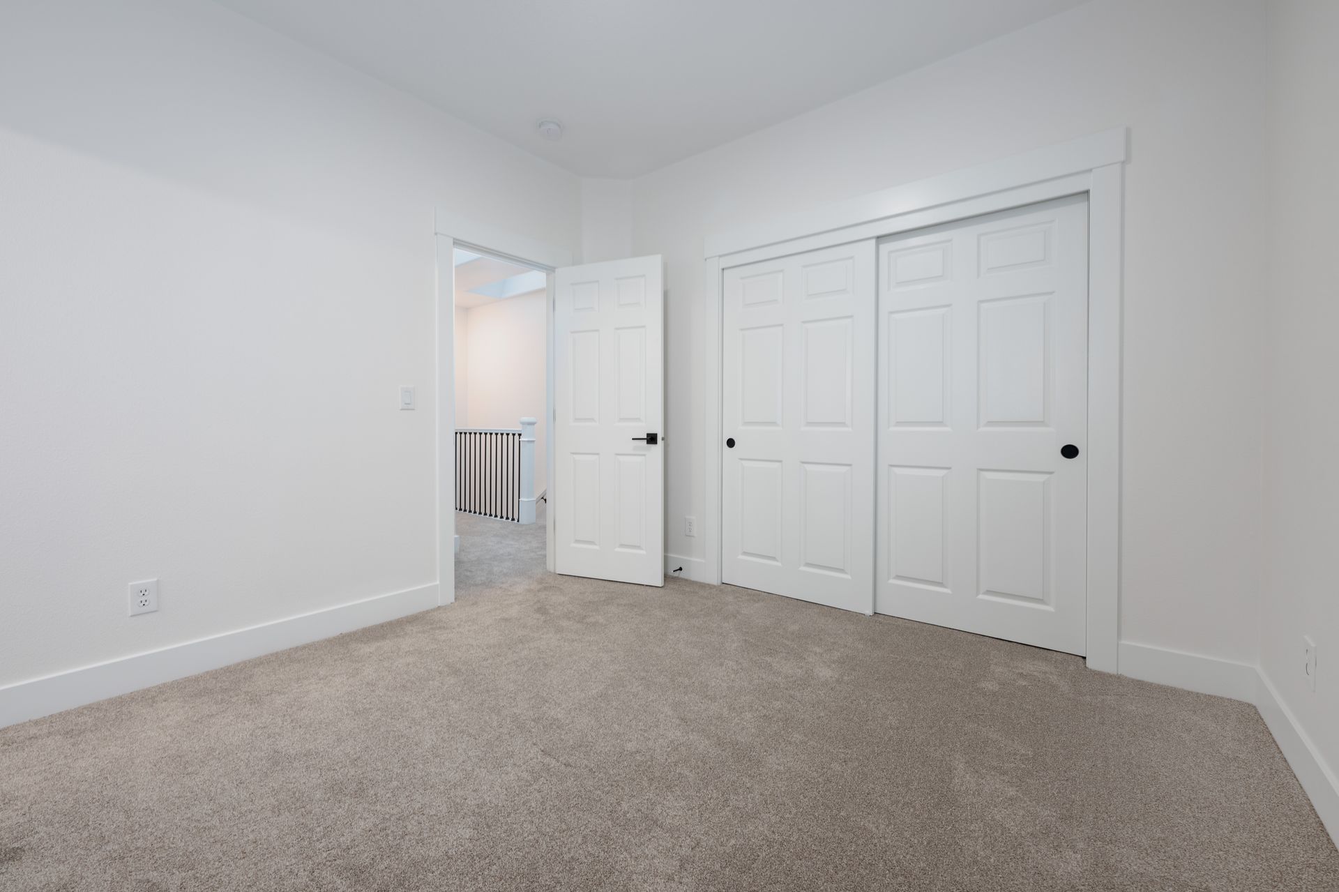 Empty bedroom with white walls, carpet, closet, and a doorway leading to a bathroom.