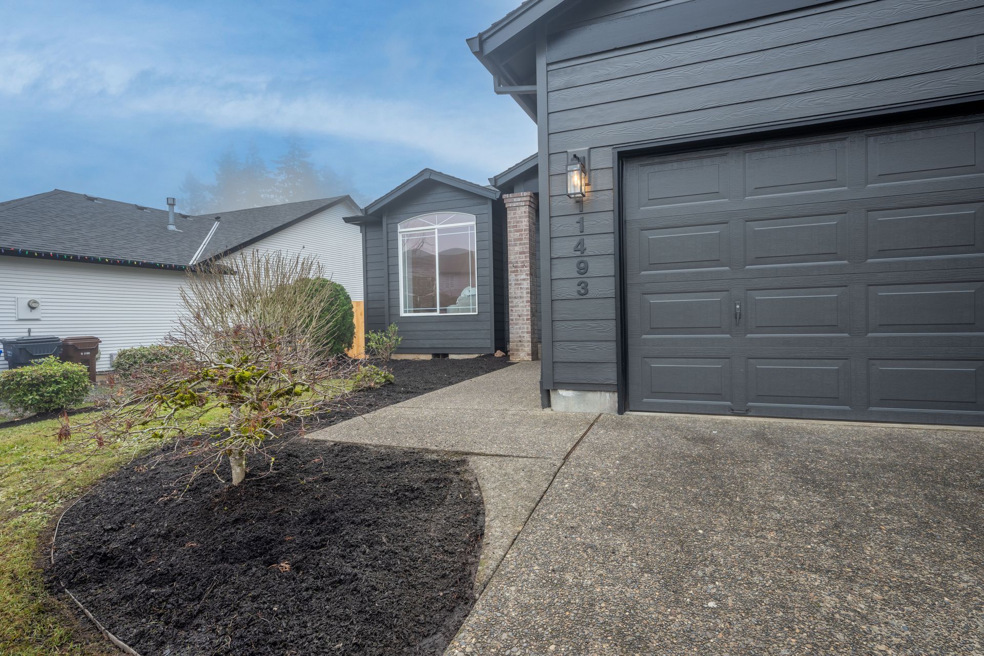 Dark gray house with a garage, path, and landscaping.