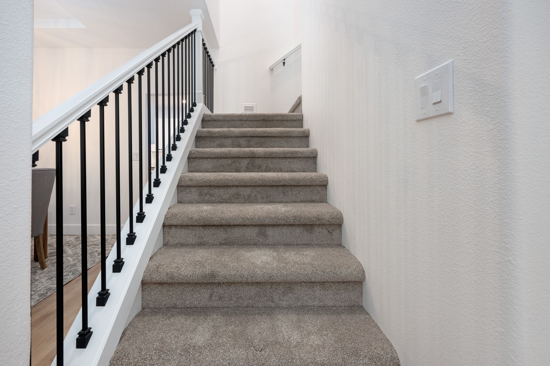 Staircase with carpeted steps, black railing, and white wall, leading upwards.