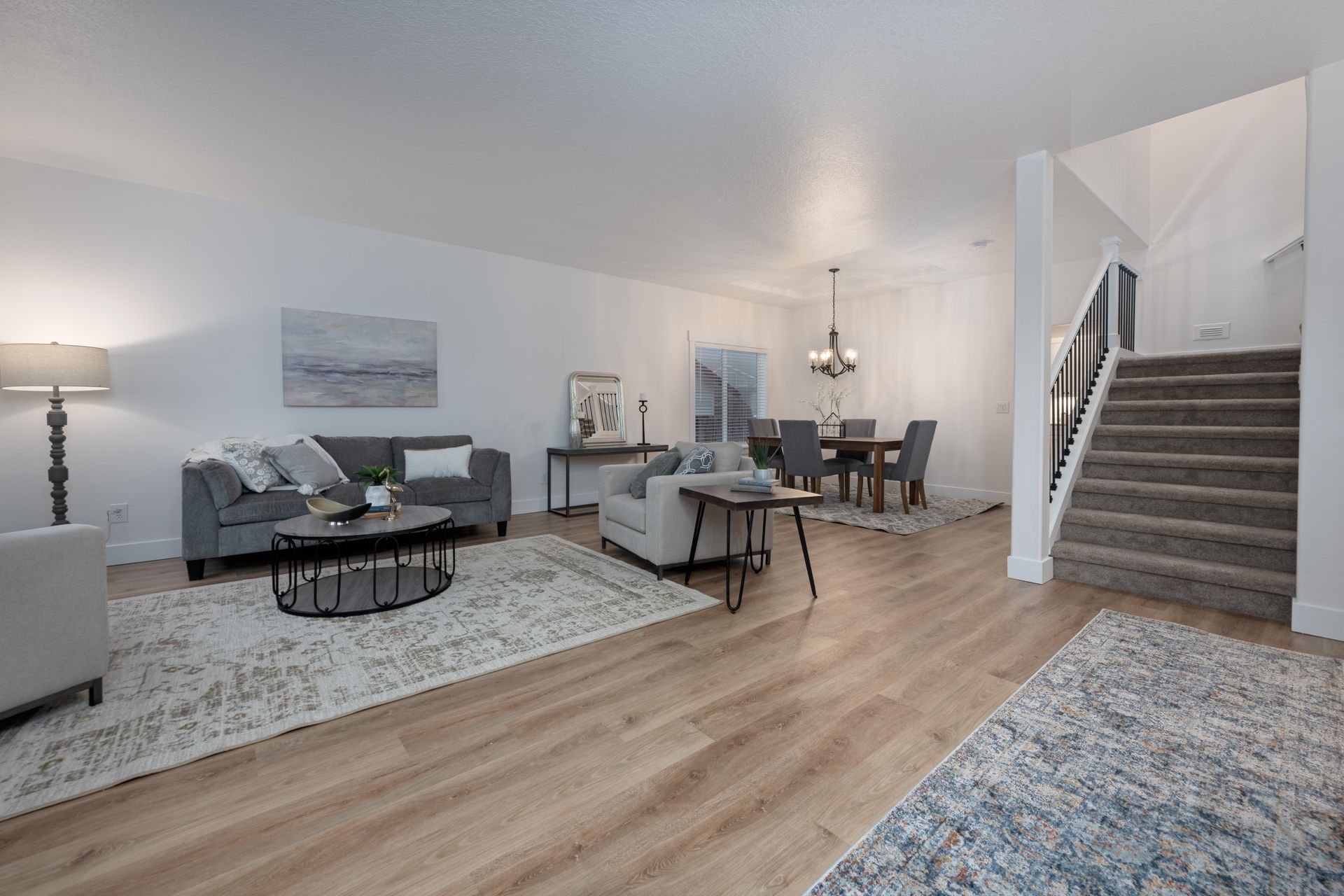 Open-concept living room with gray sofa, dining table, and staircase; neutral colors.