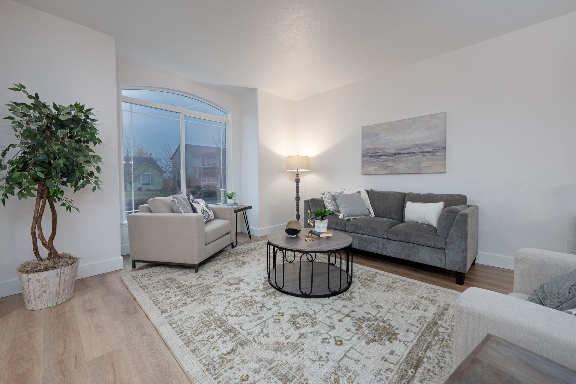 Living room with a gray sofa, beige chairs, and a round coffee table on a patterned rug.