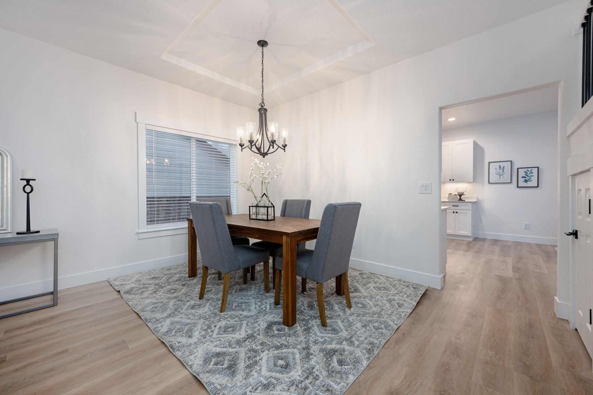 Dining room with a wooden table, gray chairs, chandelier, and rug on light wood floor.