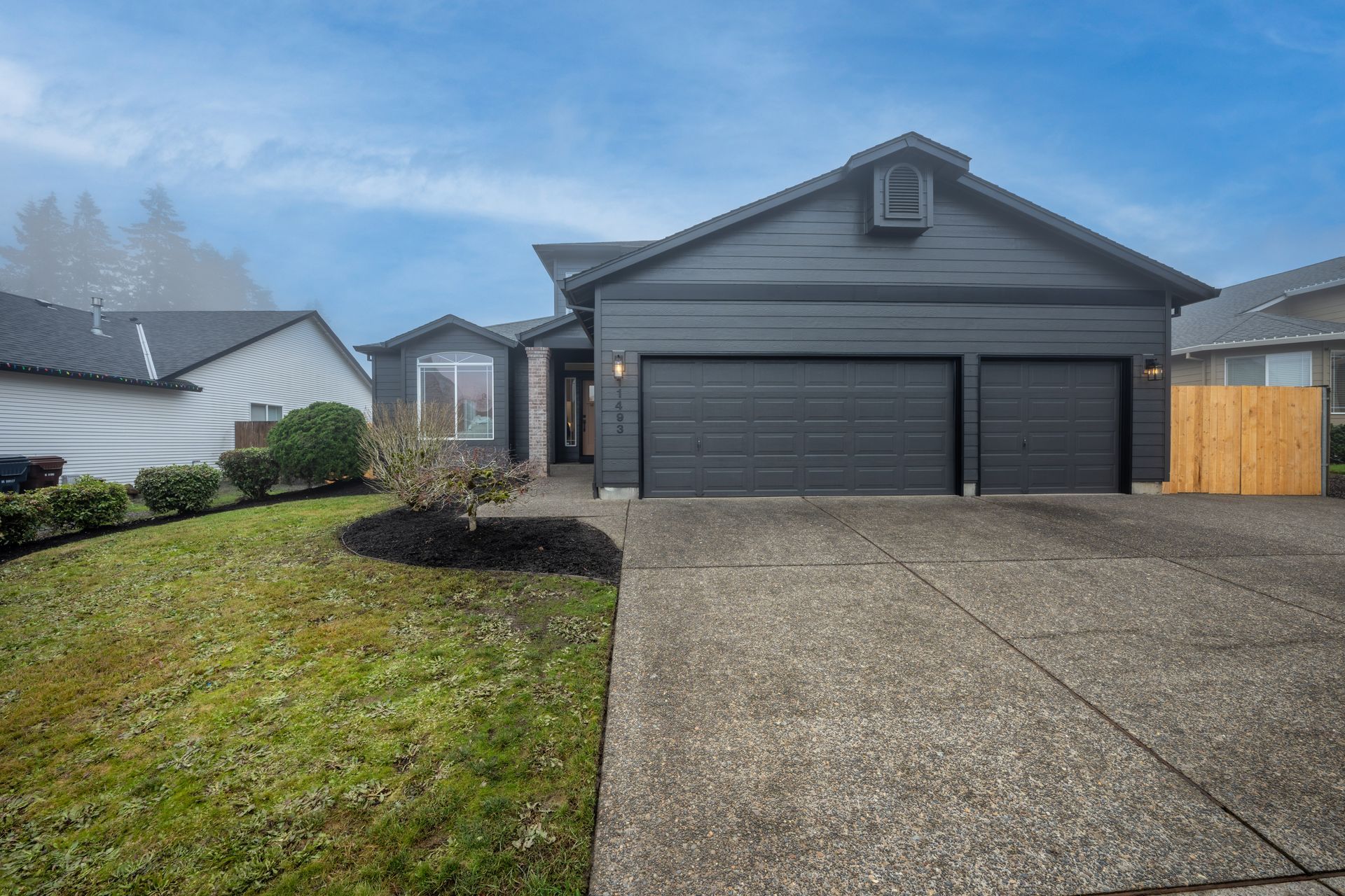Gray house with a two-car garage and concrete driveway on a cloudy day.