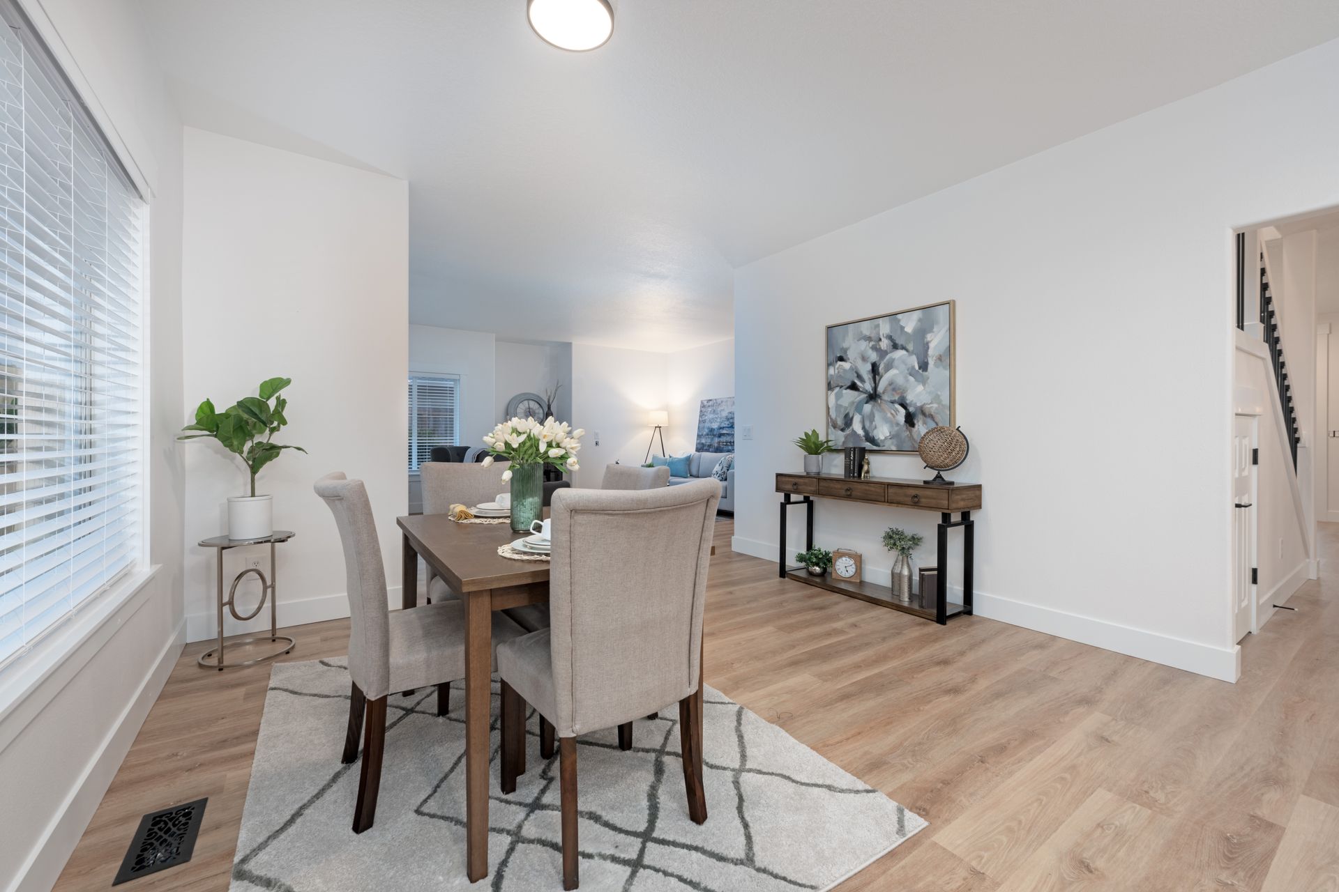 Dining room with table, chairs, rug, and console table. Light wood floors and white walls.