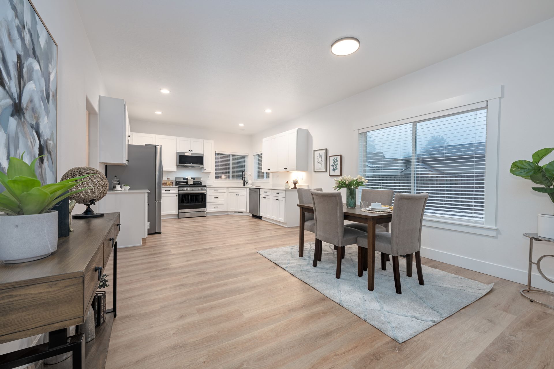 Bright, modern kitchen and dining area with light wood floors, white cabinets, and a table set for four.