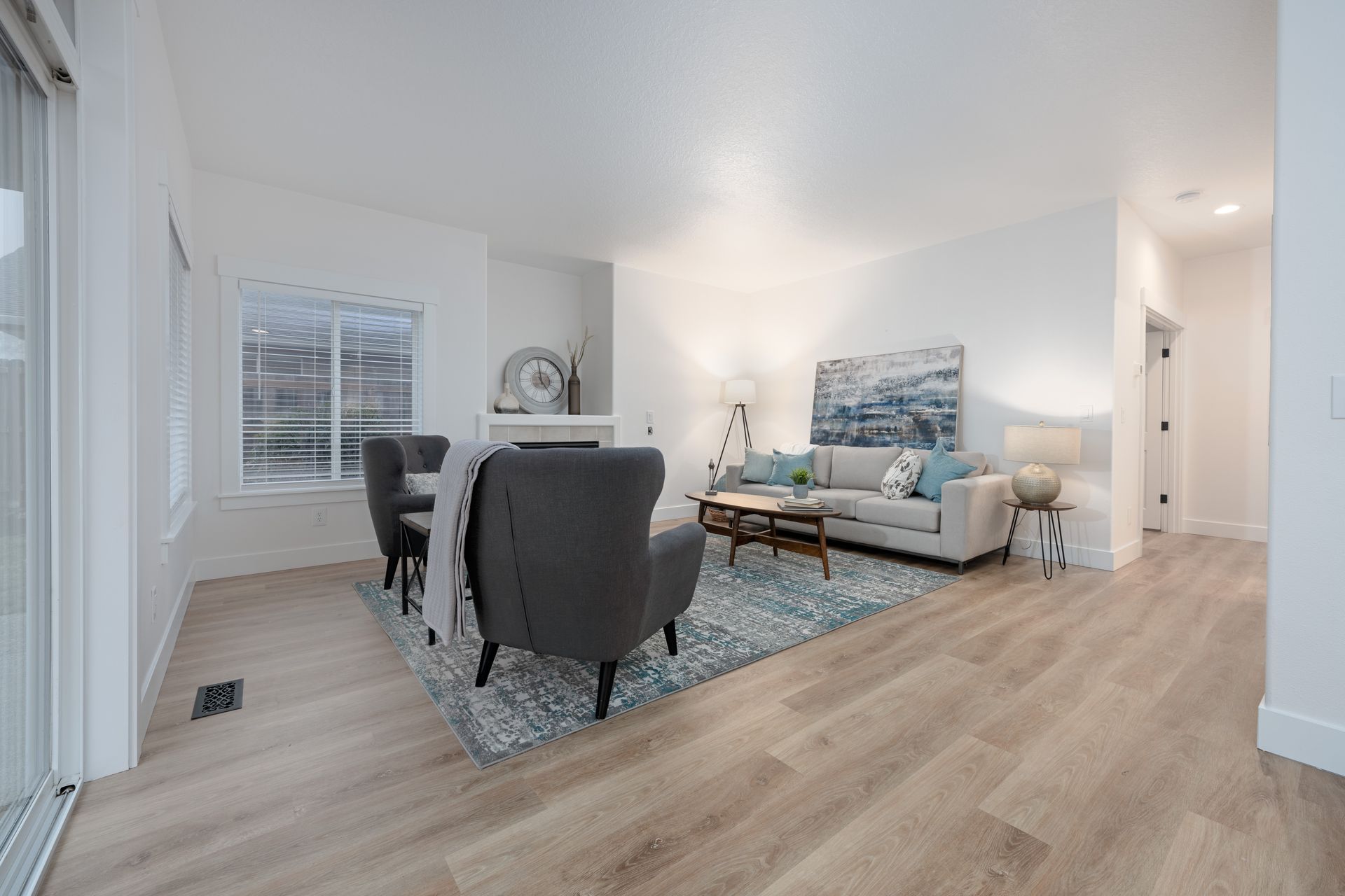 Bright living room with gray armchairs, sofa, rug, and wood-look floors.