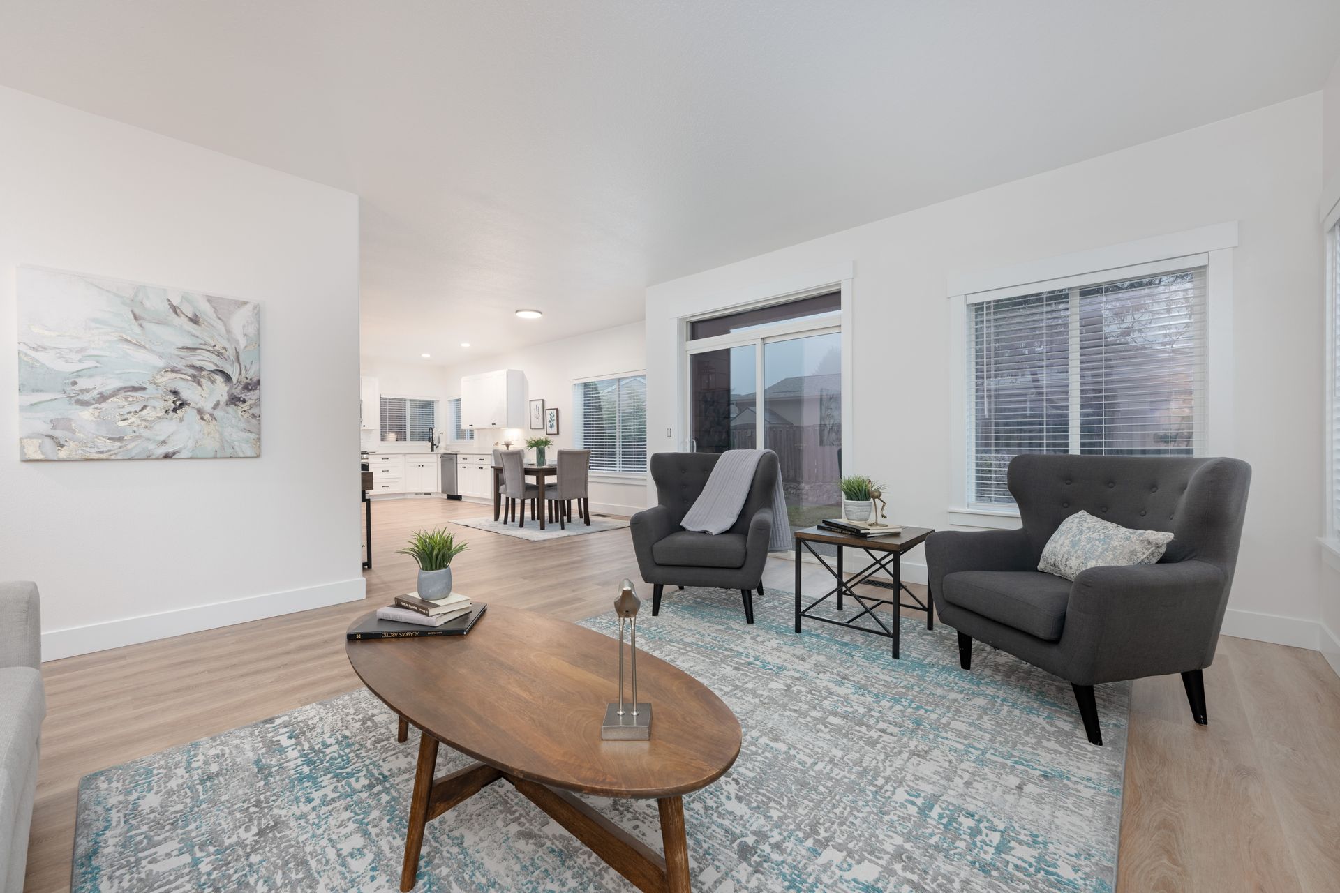 Living room with gray armchairs, oval coffee table, blue rug, and view of kitchen.