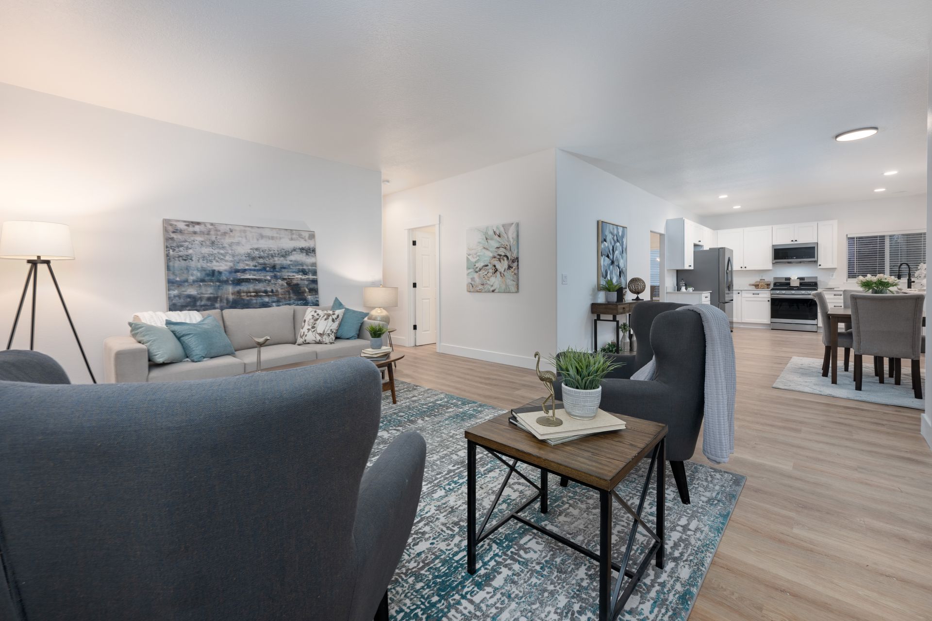 Living room with a gray sofa, armchairs, and rug. Open to a kitchen and dining area.