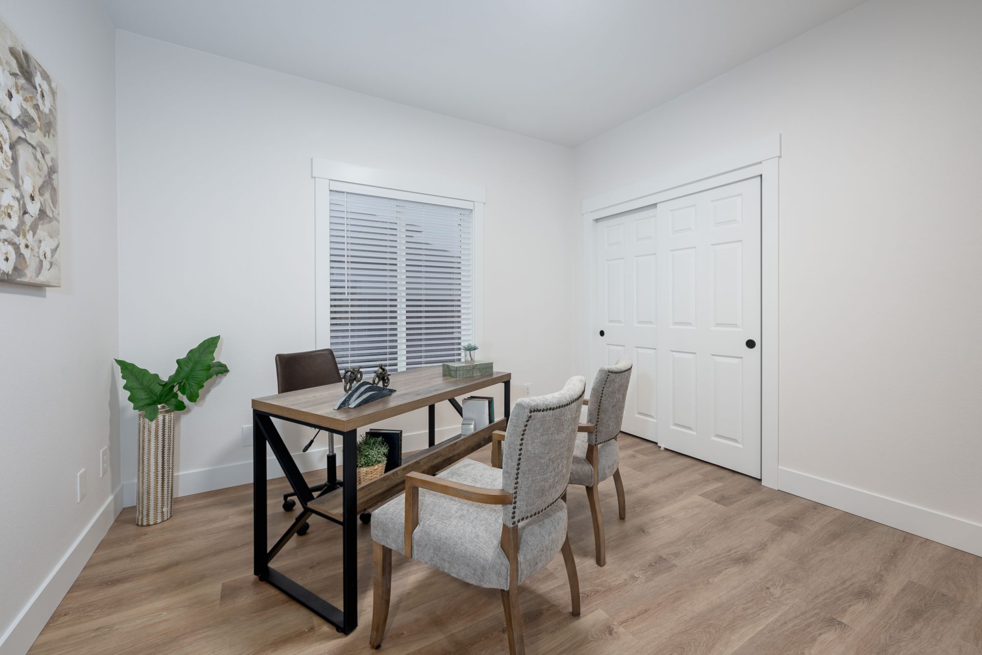 A modern office with desk, chairs, white walls, wooden floor, and sliding closet doors.