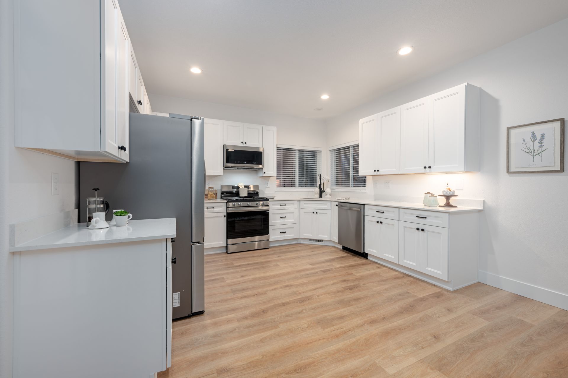 White kitchen with stainless steel appliances and light wood floors.