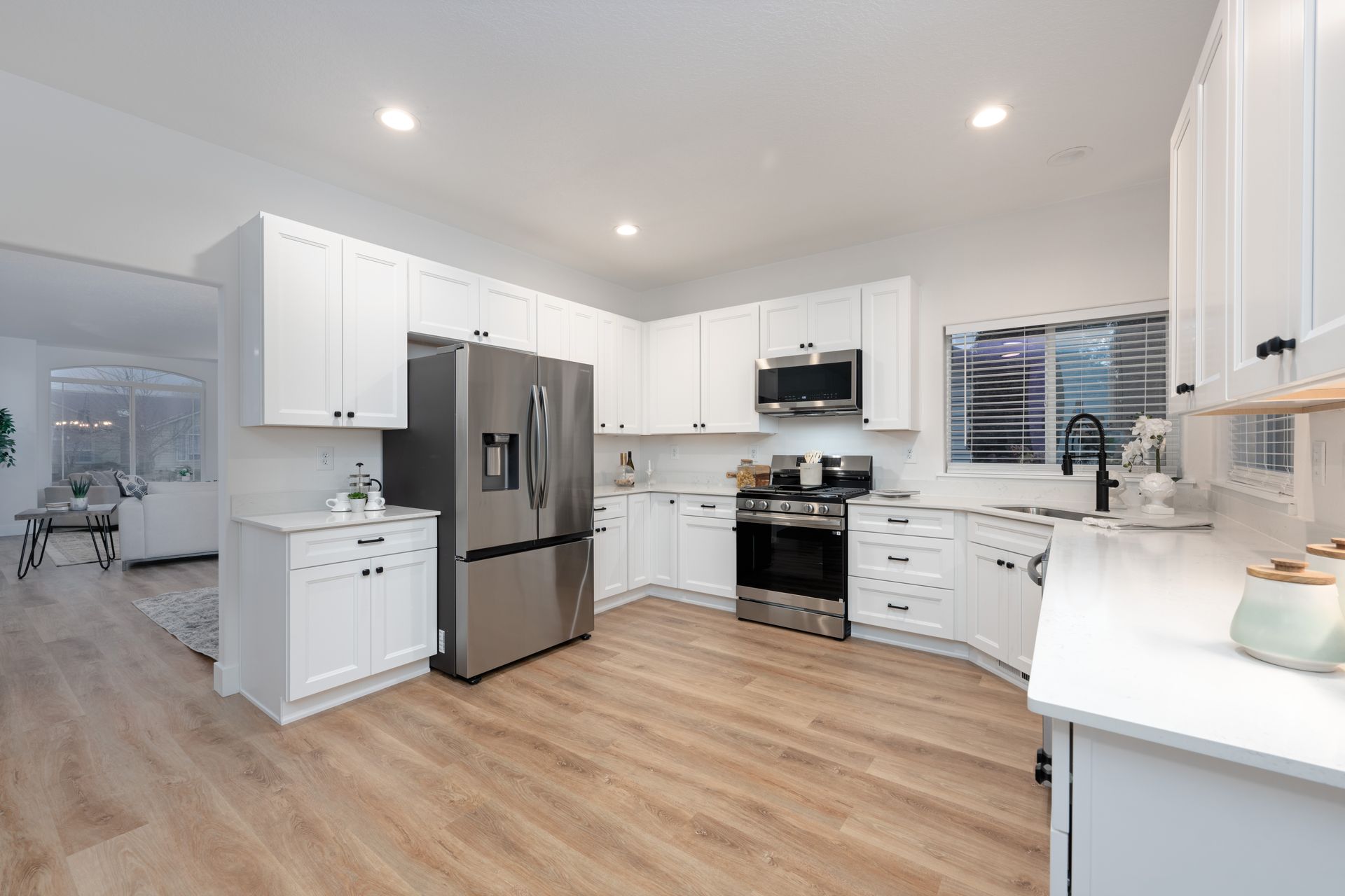 Modern white kitchen with stainless steel appliances and light wood floors.