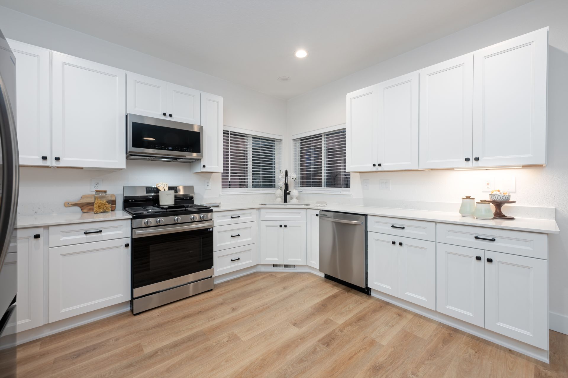 White kitchen with stainless steel appliances and light wood floor.