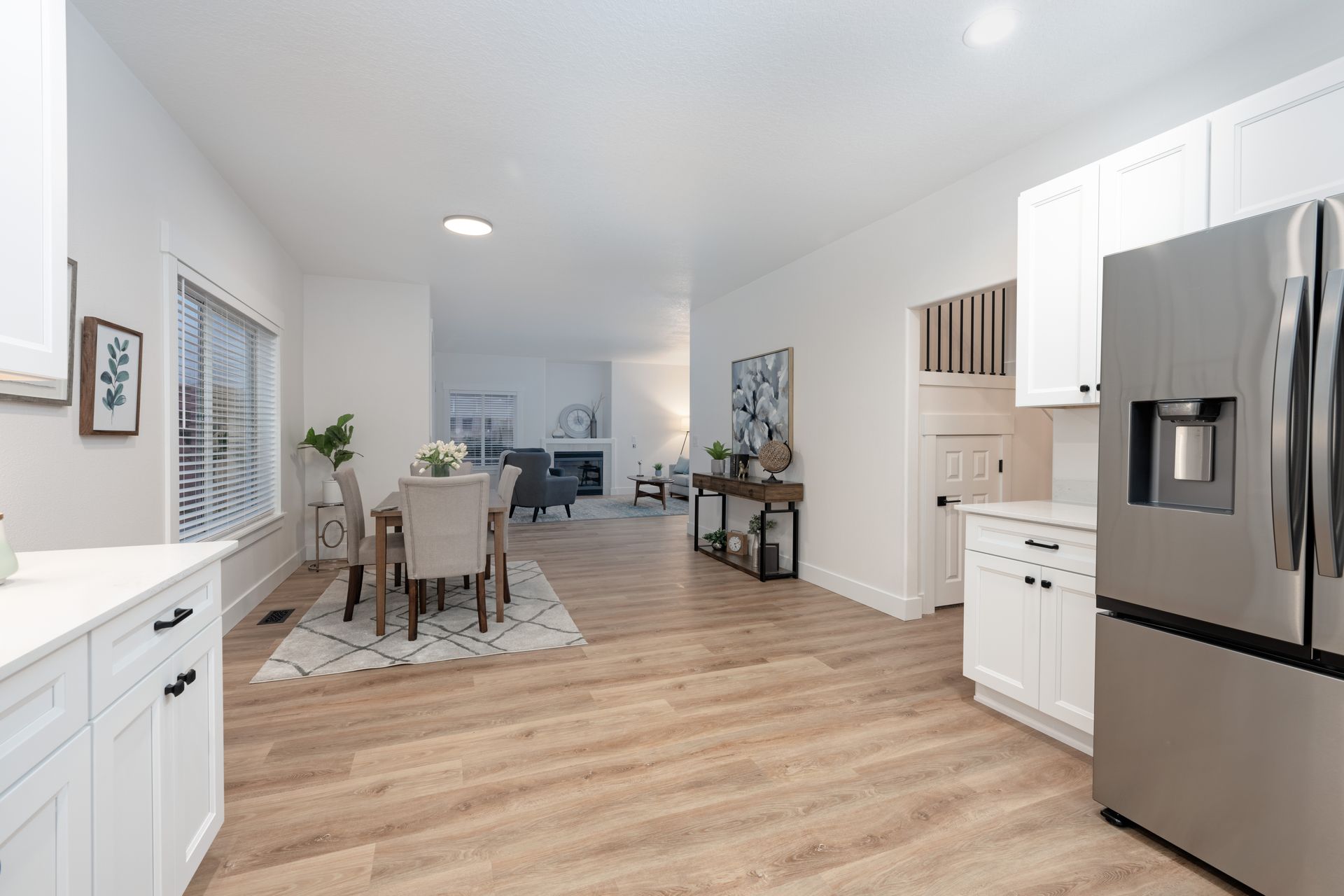 Open-concept kitchen and dining area with wood floors, white cabinets, and stainless steel refrigerator.