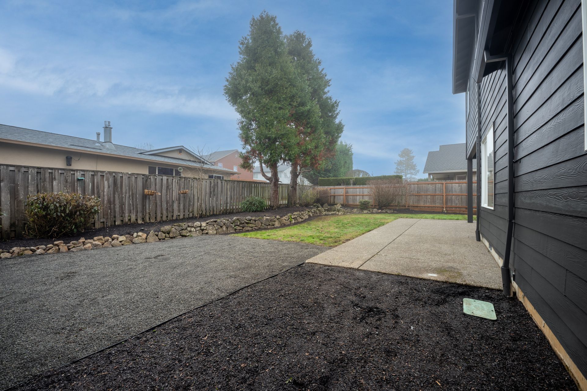 Backyard with gravel path, patio, lawn, and fence under overcast sky.