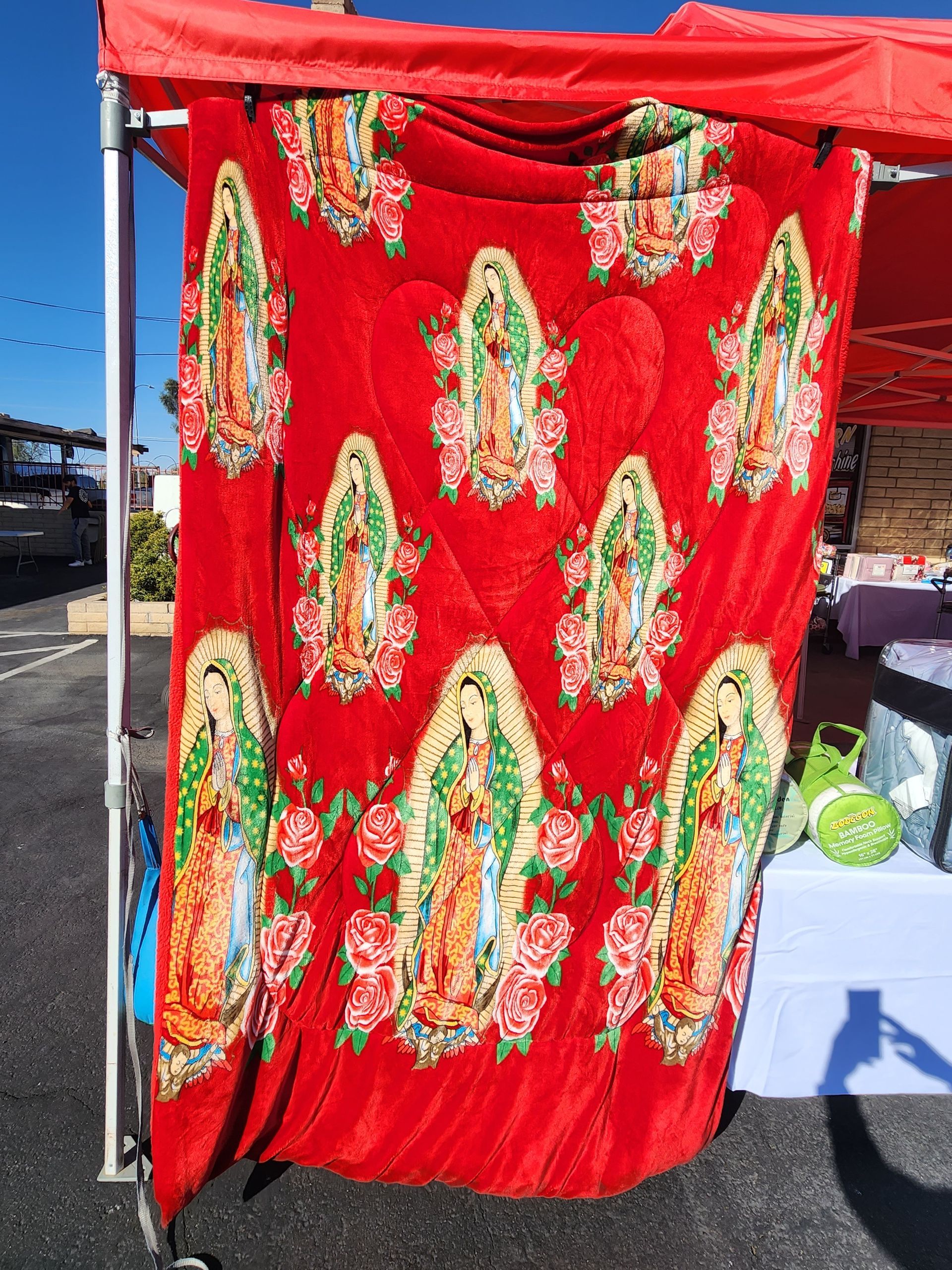 a red blanket with a picture of the virgin mary on it is hanging under a tent .