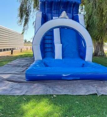 a blue and white bouncy castle water slide is sitting on top of a tarp in the grass .