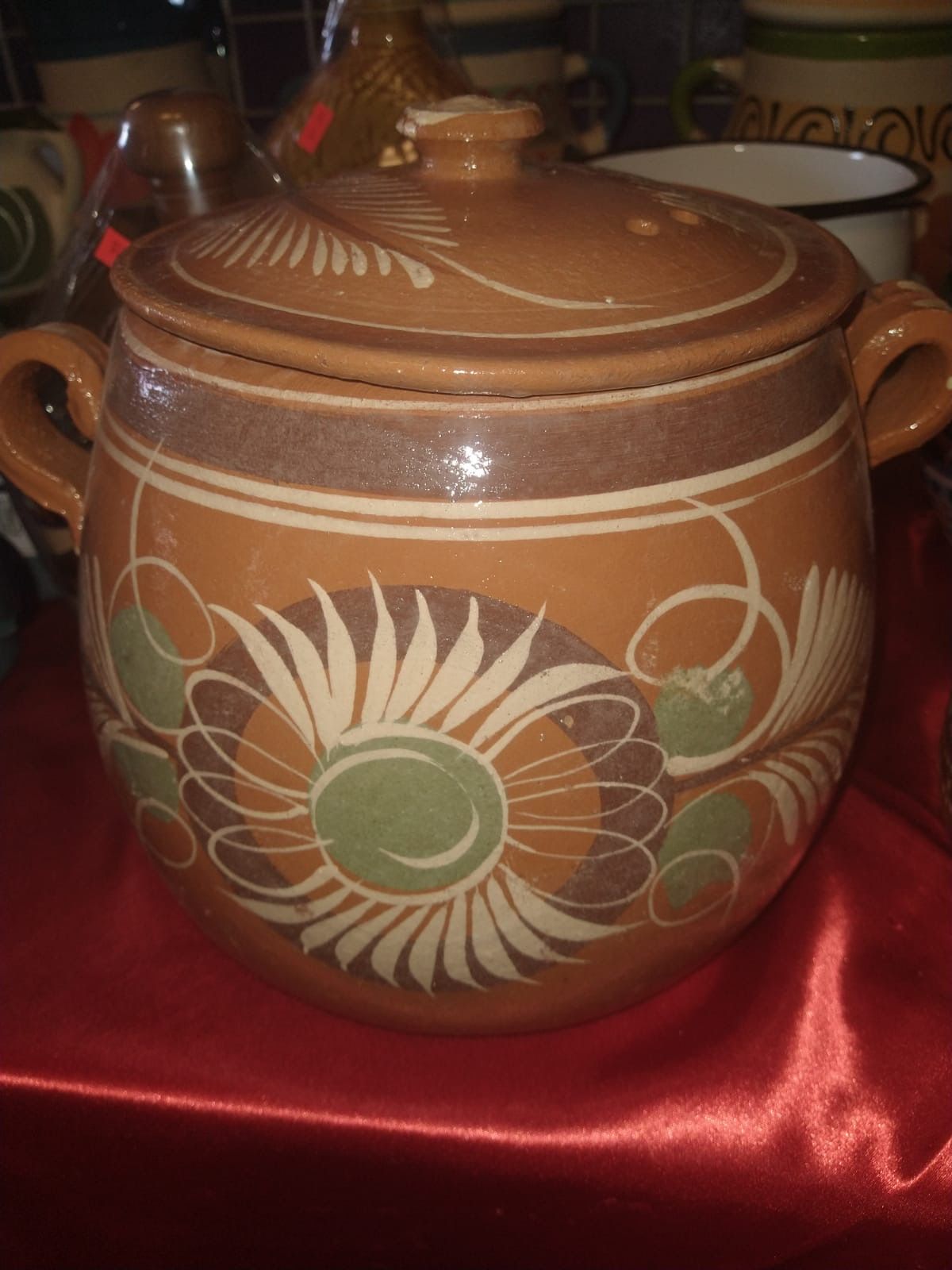 a clay pot with a lid and handles is sitting on a red cloth .