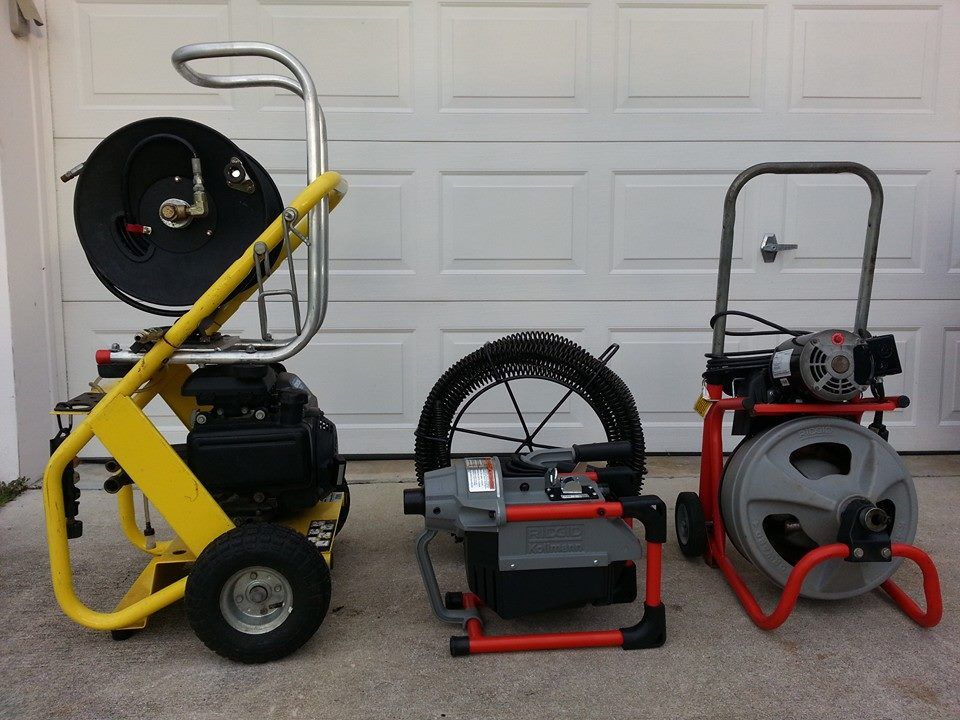Three drain cleaners are lined up in front of a garage door