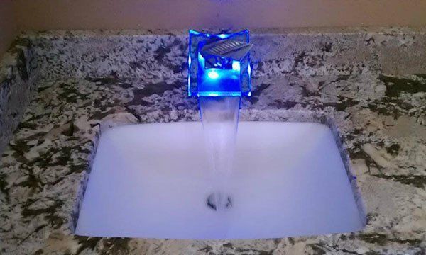 A bathroom sink with a blue light on the faucet.