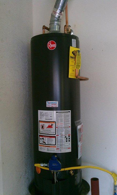 A black water heater is sitting in a corner of a room.