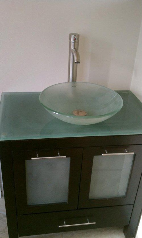 A bathroom vanity with a glass sink and faucet