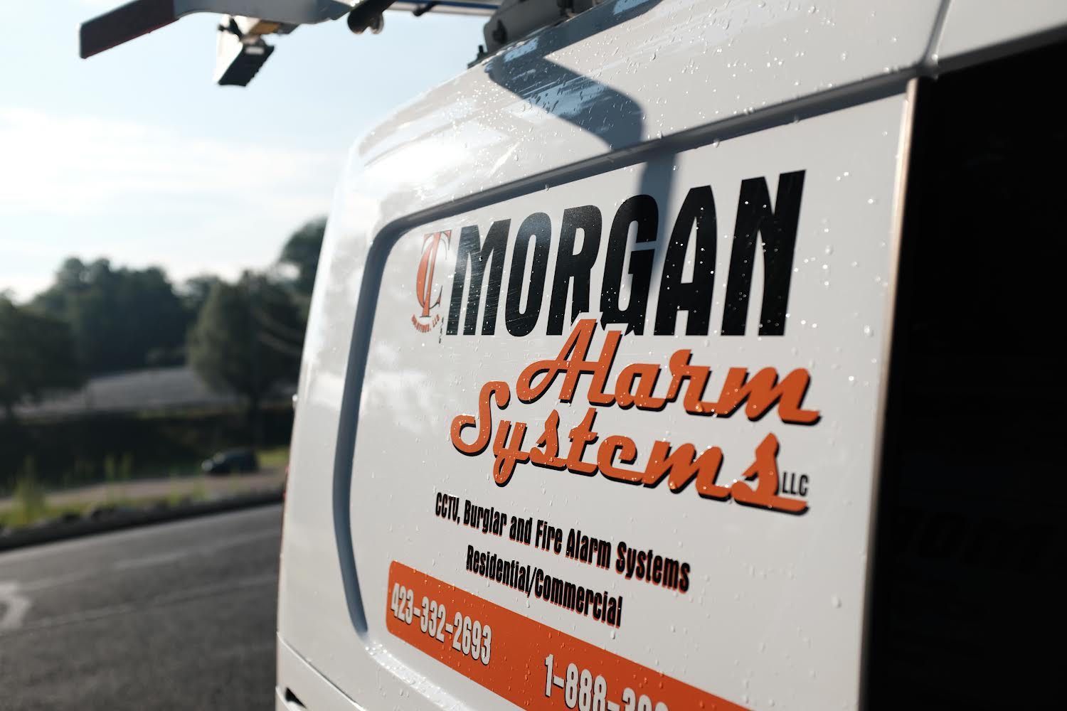 Morgan Alarm Systems logo on a white vehicle door, parked outdoors.