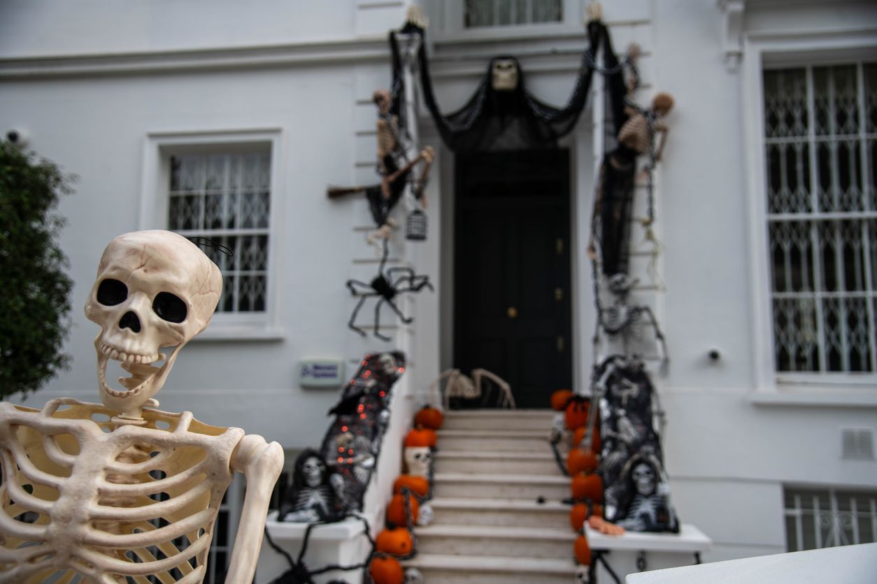 Skeleton Halloween display at a house entrance with black cobweb decorations and pumpkins