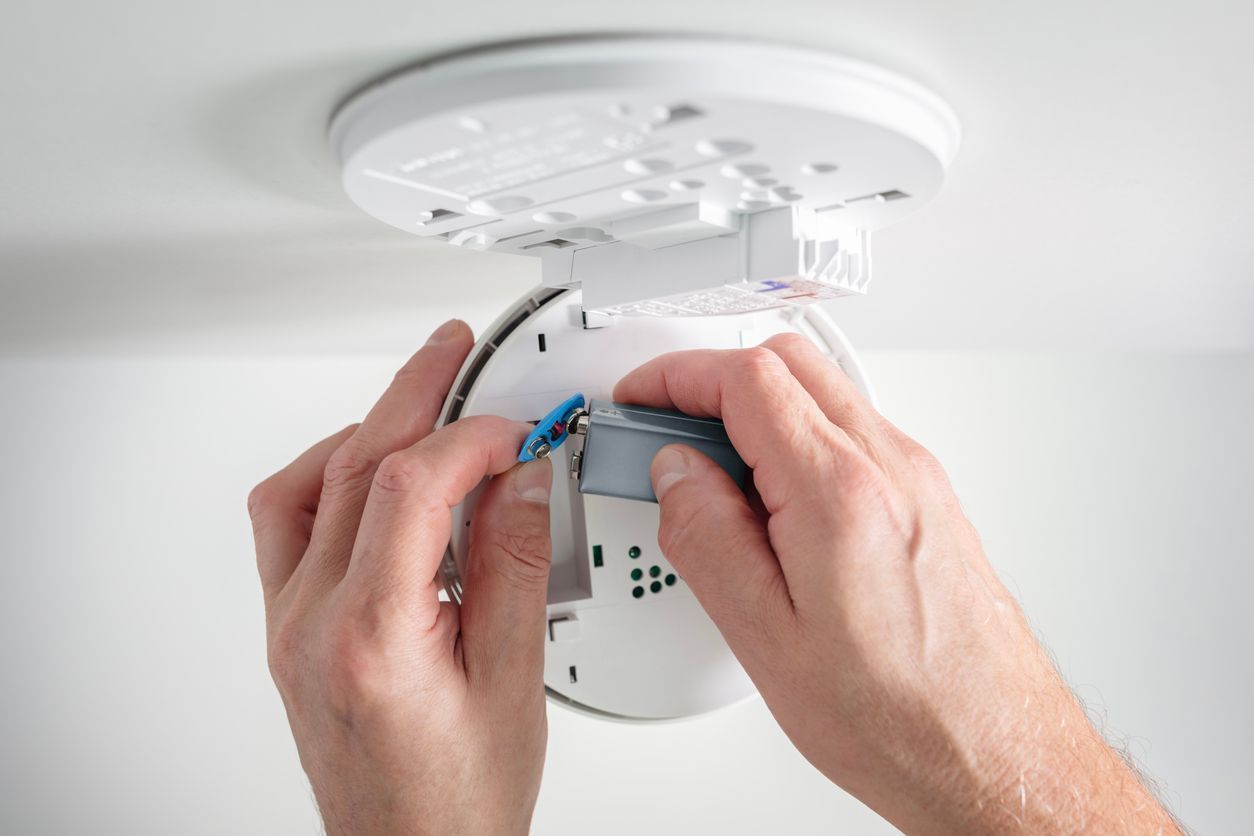 Hands installing a smoke detector on a ceiling mount with a screwdriver