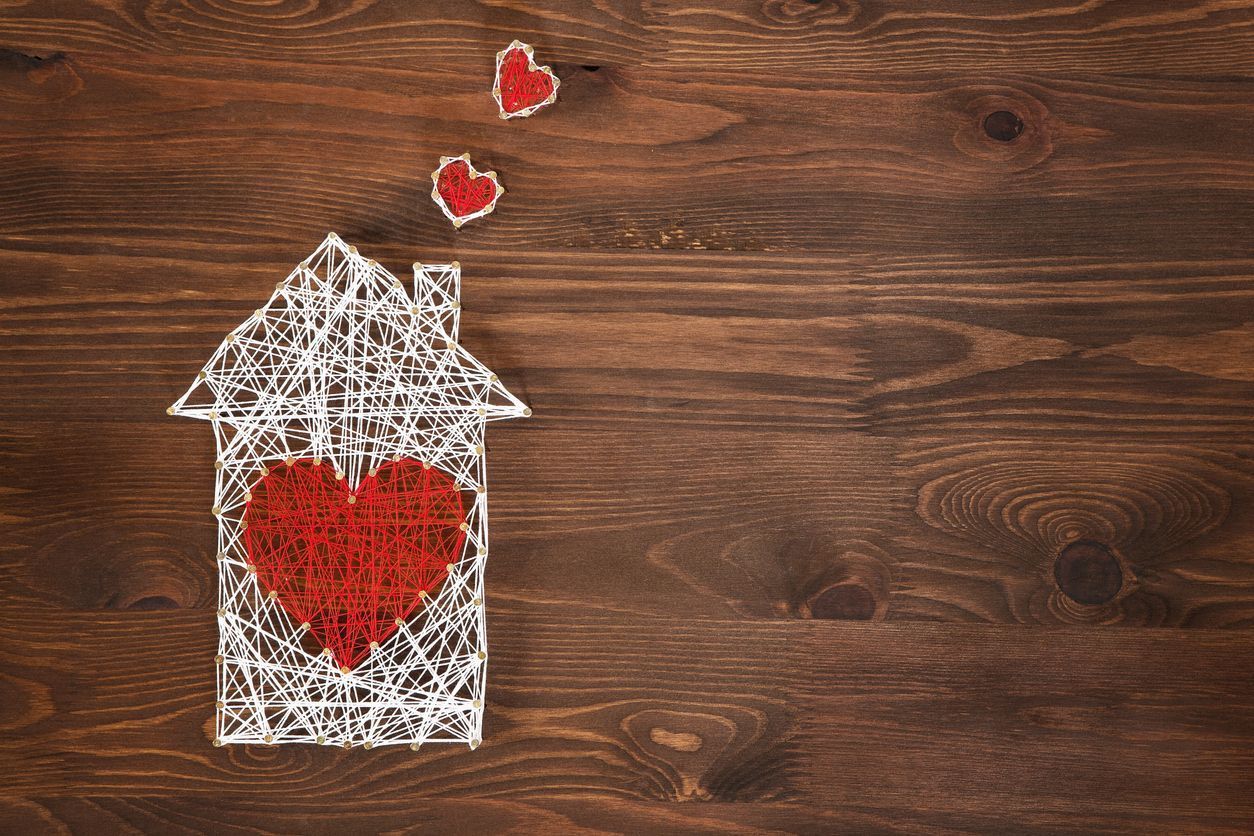 White doodle house with a red heart and floating hearts on a wooden background