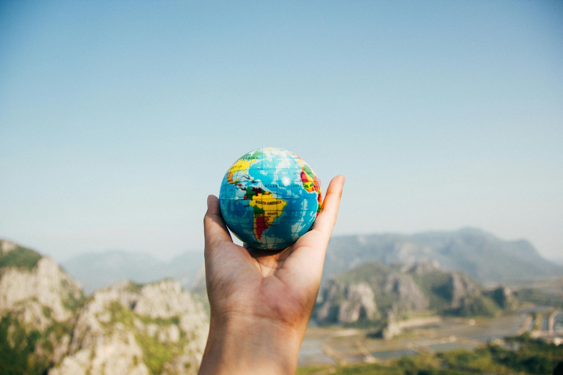 Hand holding a small globe with mountains and sky in the background