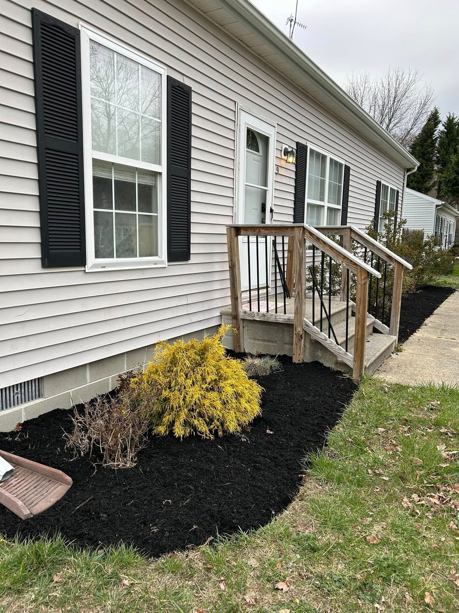 A mobile home with black shutters and black mulch in front of it.
