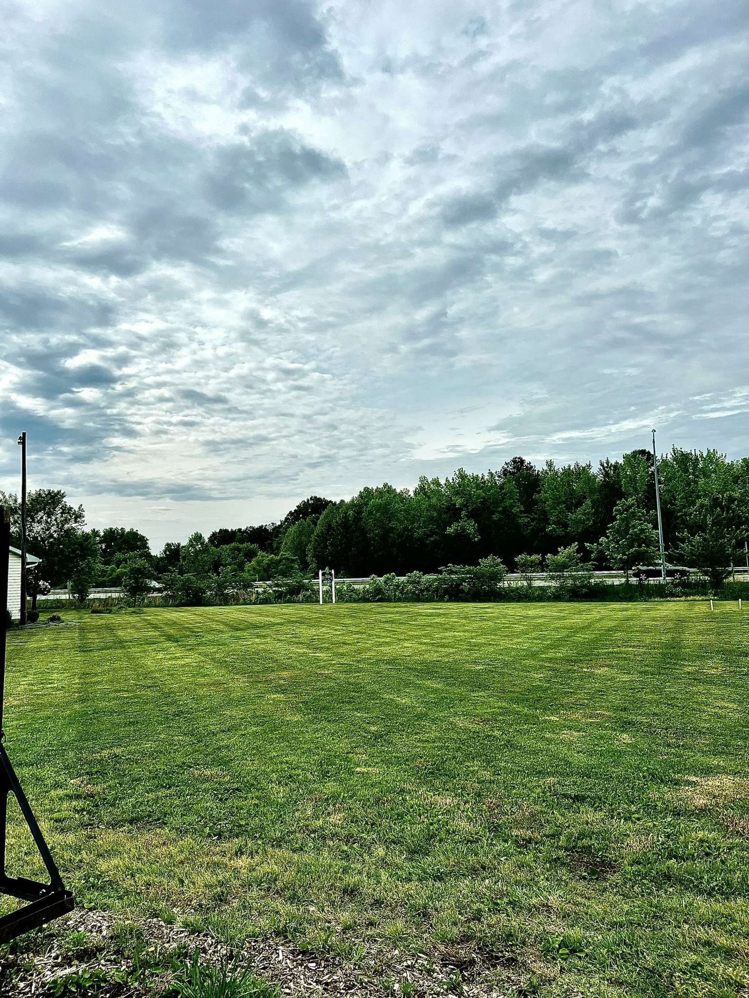A large grassy field with trees in the background and a cloudy sky