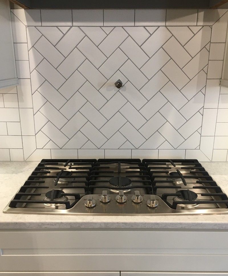 A stove top oven with a herringbone tile backsplash