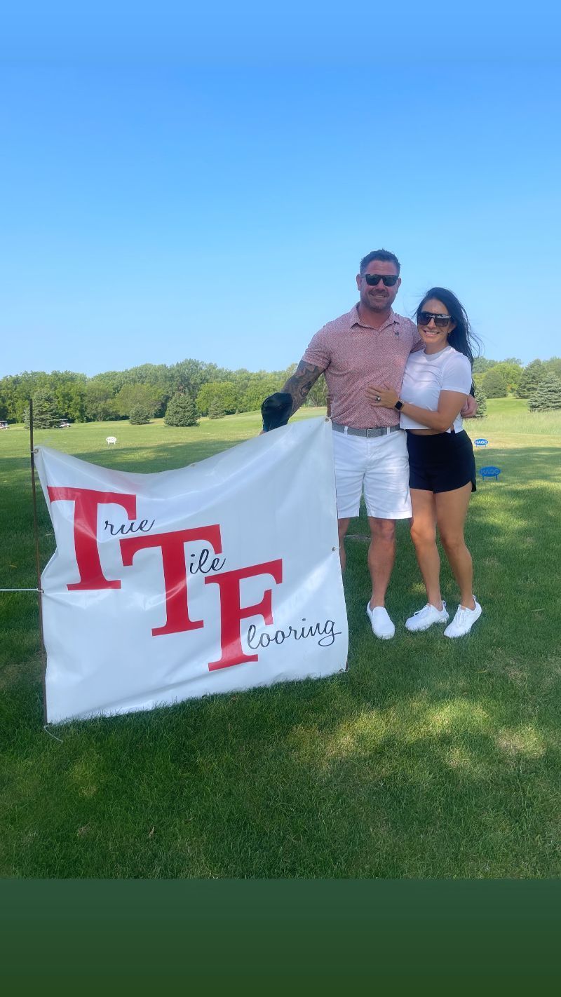 A man and a woman are standing on a golf course holding a flag.