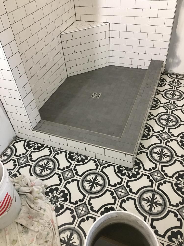 A shower stall with a black and white tile floor and white brick walls.