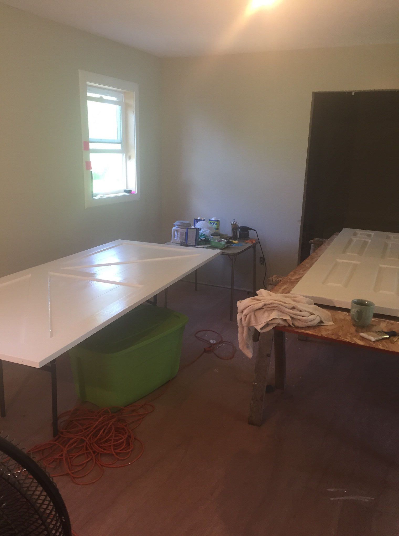 Room with two white doors on tables, painting supplies, a window, and an extension cord.