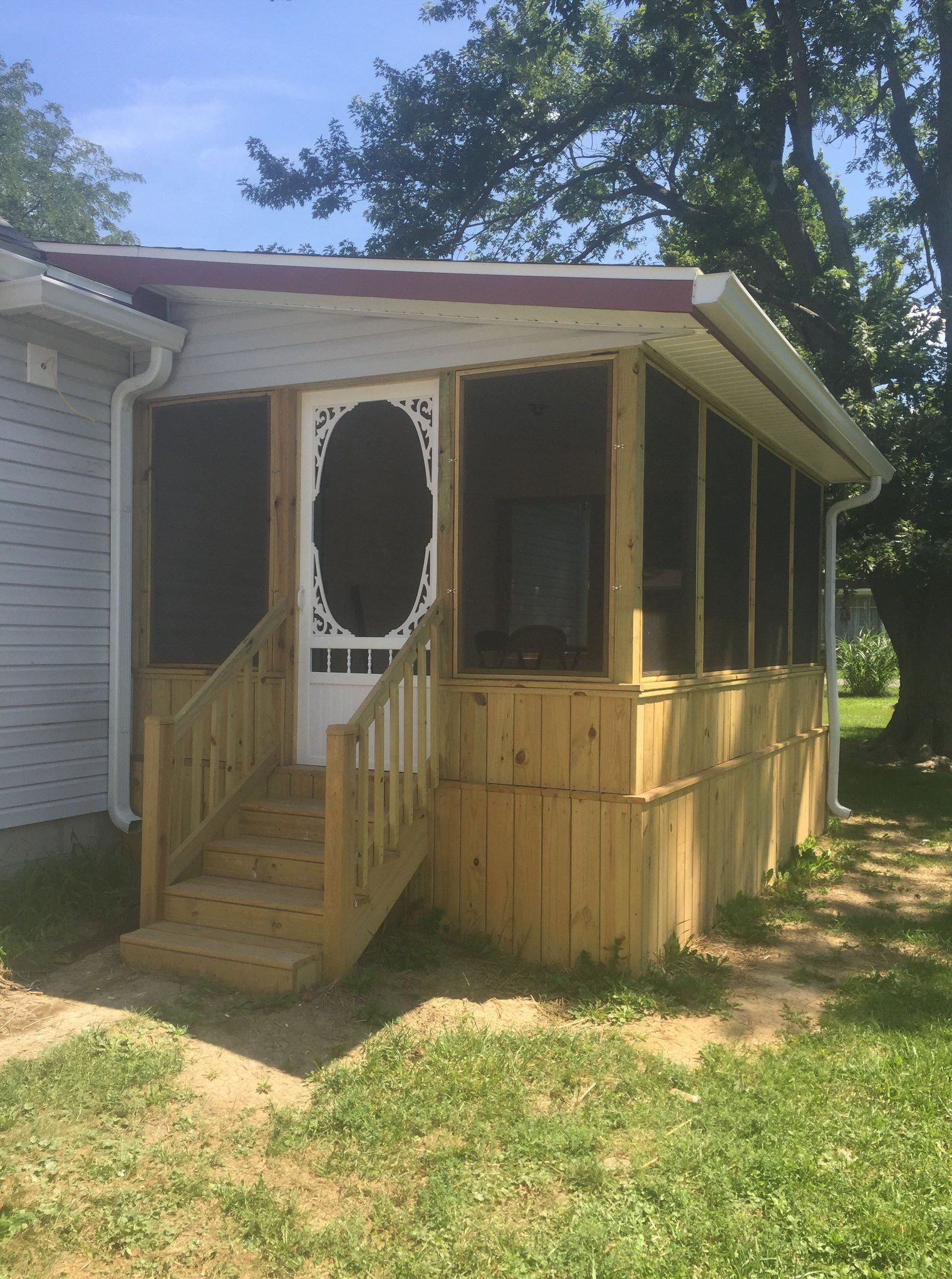 Screened-in porch addition with wooden steps, siding, and door, attached to a house with a grassy yard.