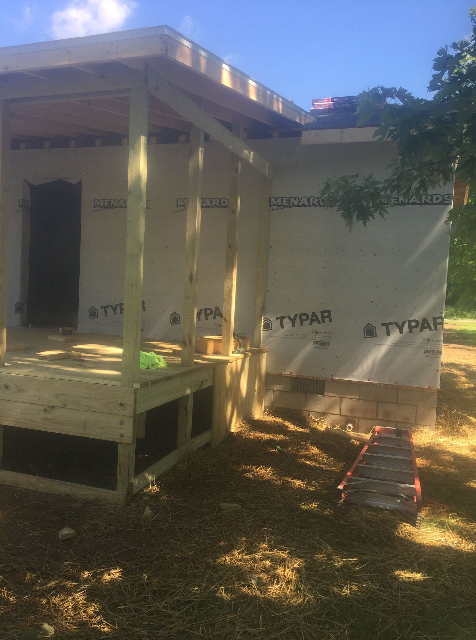 Exterior view of a building under construction, featuring wooden framing, a porch, and Typar wrap.