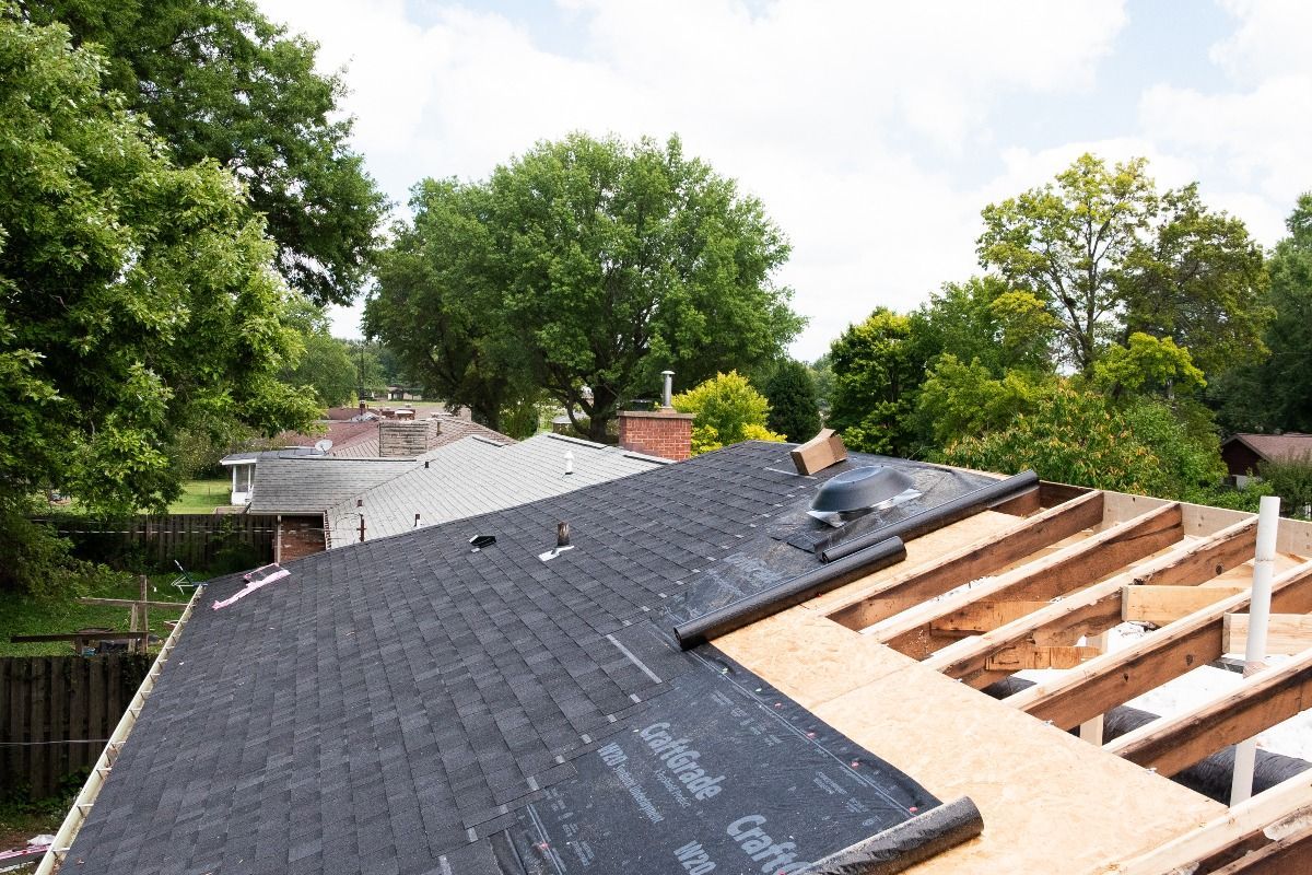 Roof partially covered with black shingles, revealing exposed wooden beams.