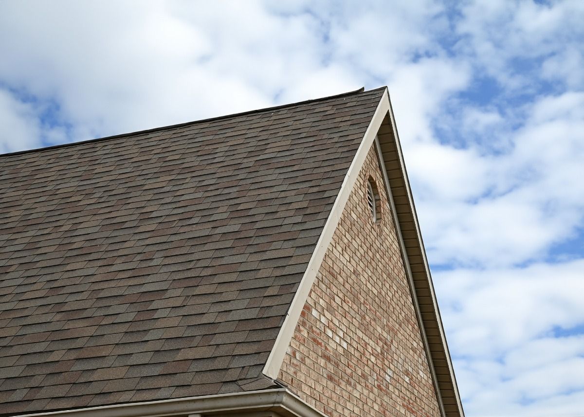 Brown shingled roof and brick facade against a blue sky with clouds.
