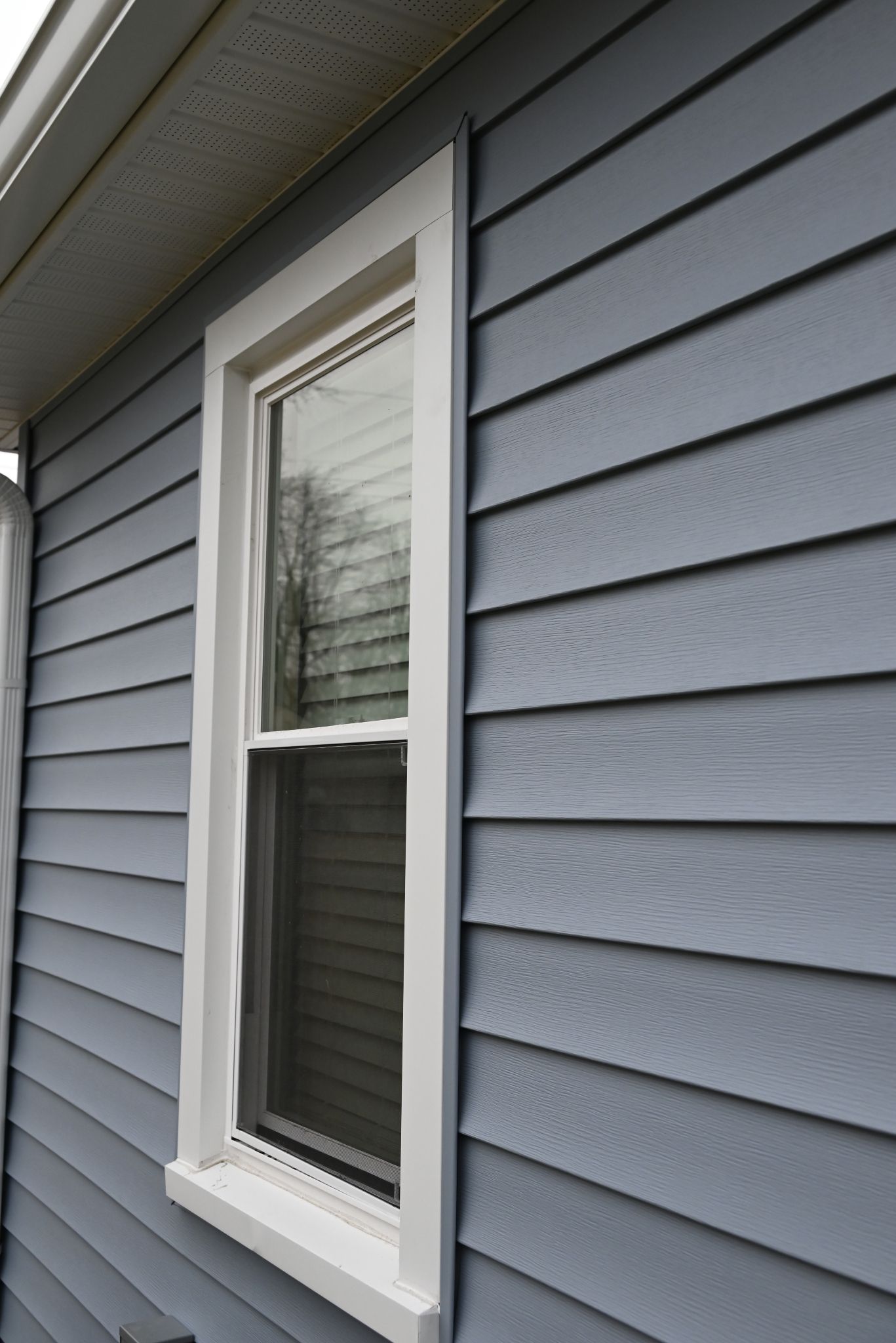 Blue siding with white trim around a tall, narrow window.